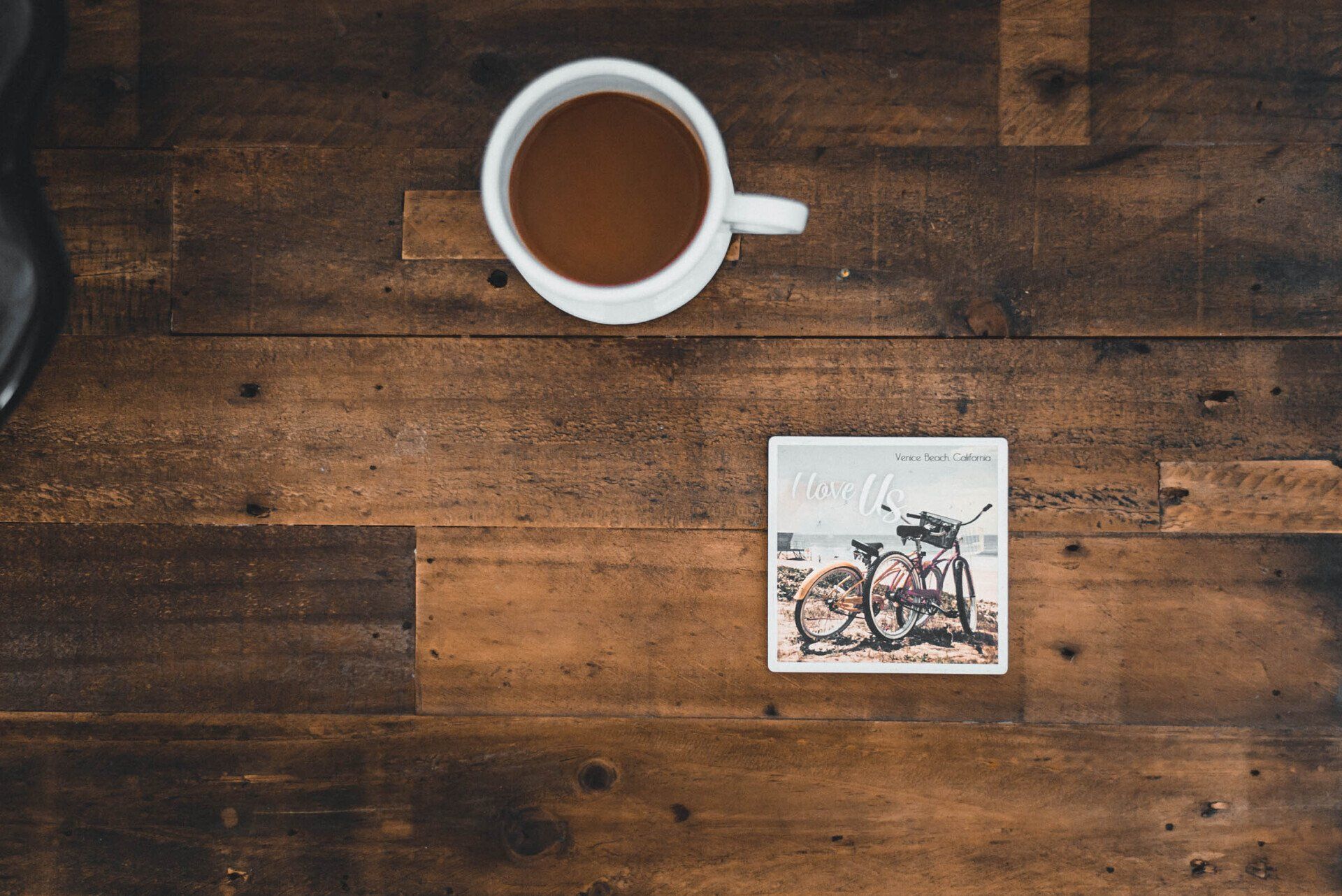 A cup of coffee and a postcard on a wooden table.