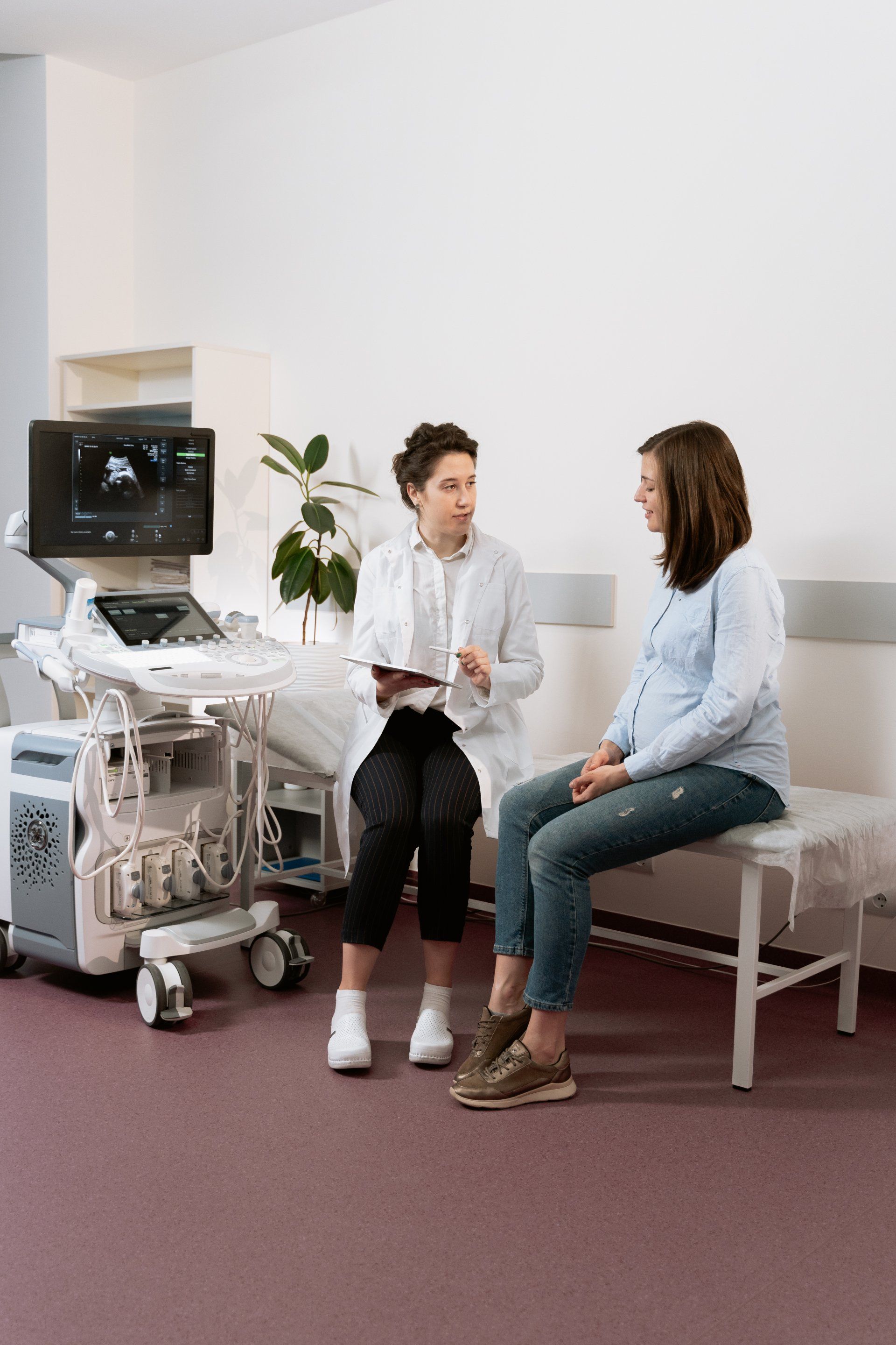 A pregnant woman is sitting on a bench talking to a doctor. Consulting in a doctors office
