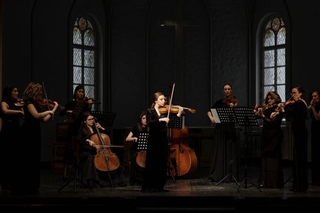 A woman is playing a violin in front of a large orchestra.