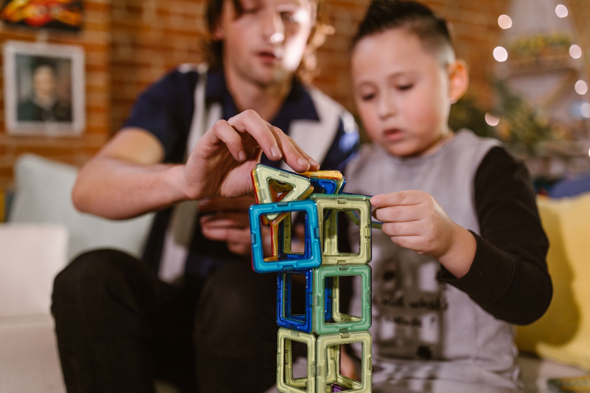 A man and a boy are playing with magnetic blocks on a couch.