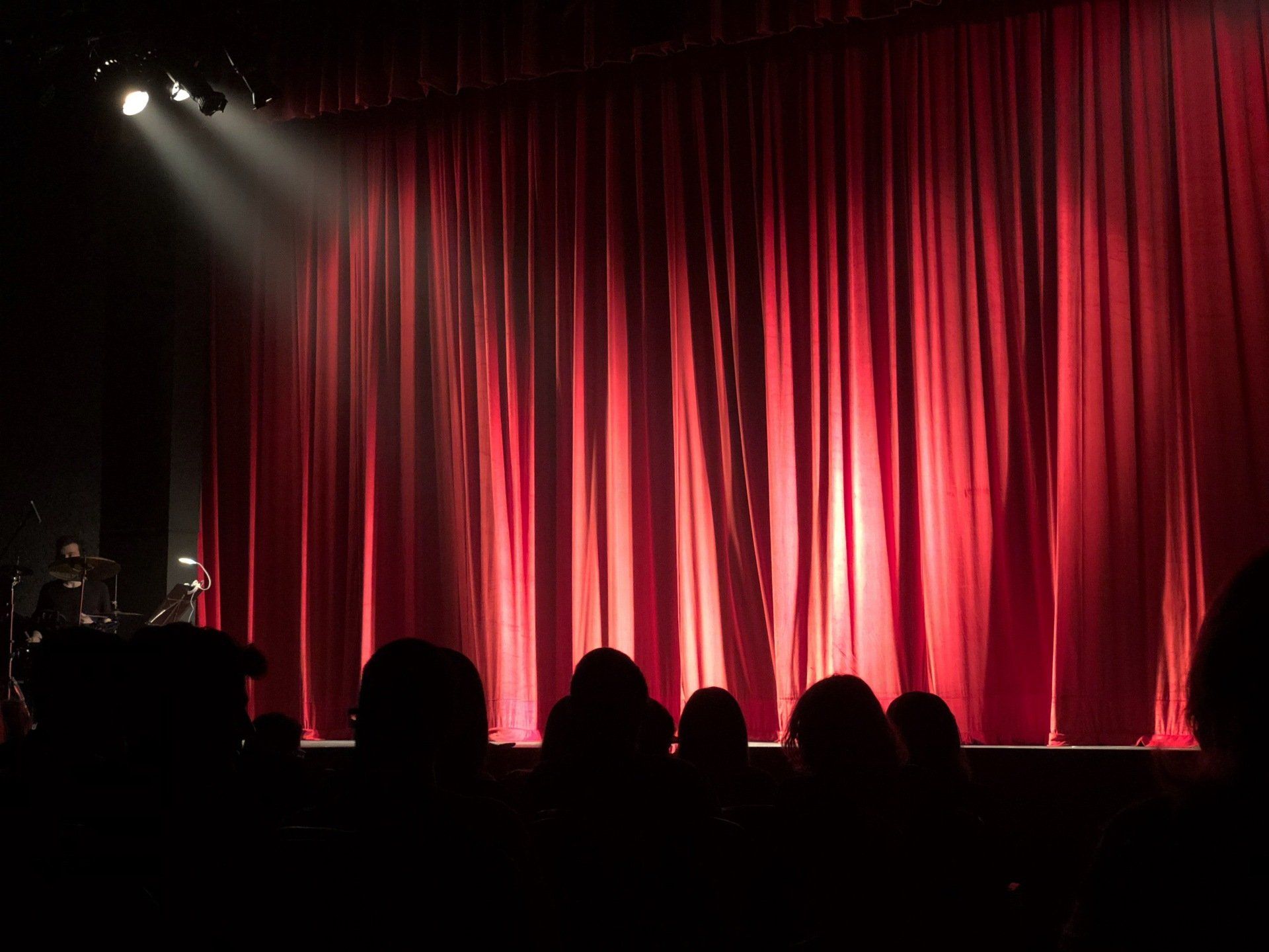 a group of people are sitting in front of a stage with red curtains .