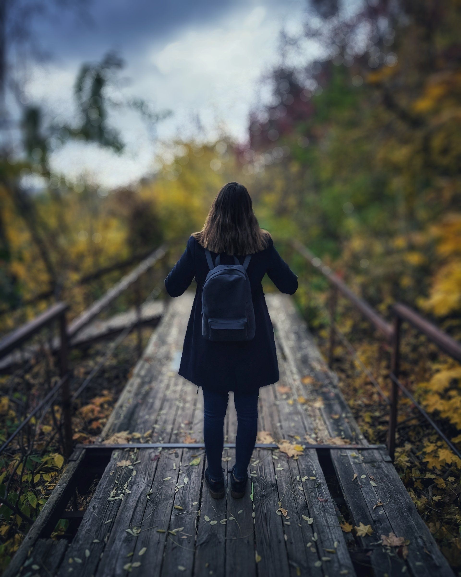 A woman with a backpack is walking across a wooden bridge.