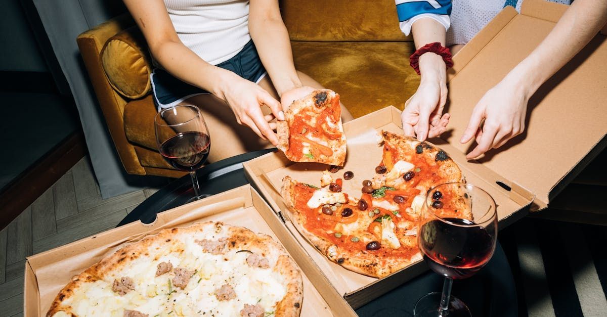 Two women are sitting at a table eating pizza and drinking wine.