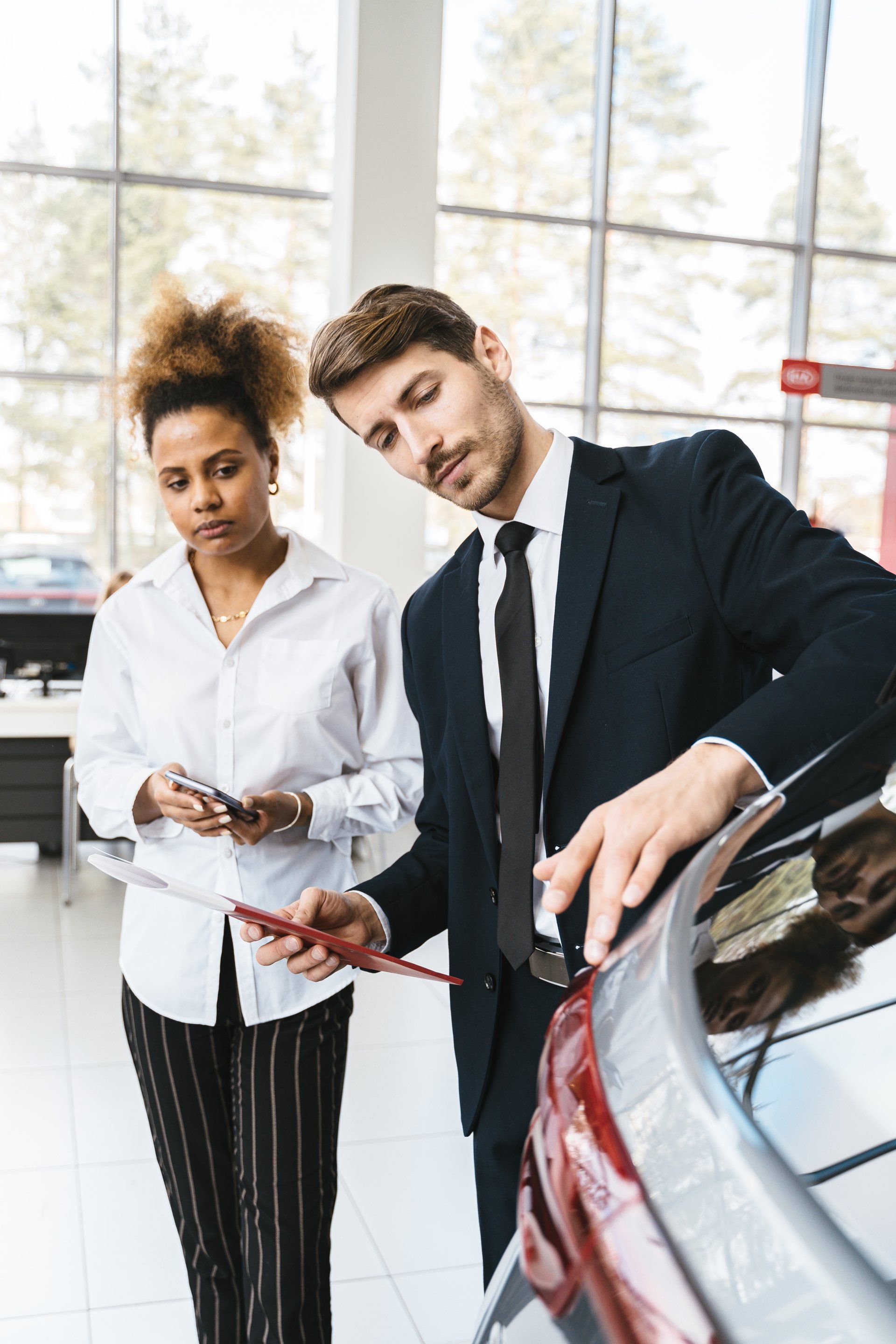 A man and a woman are looking at a car in a showroom.