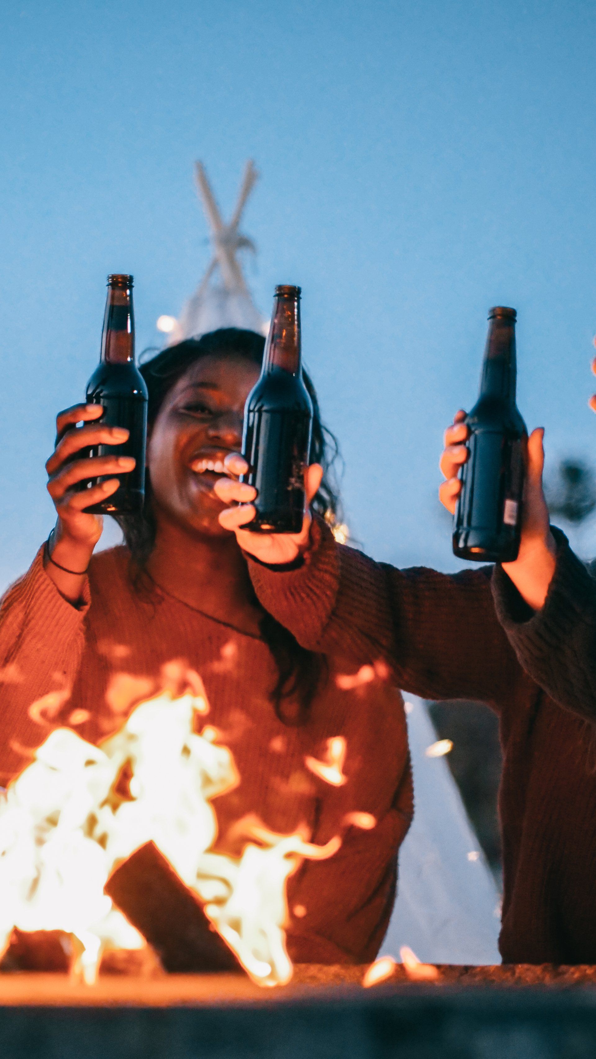 A group of people are toasting with beer bottles in front of a fire.