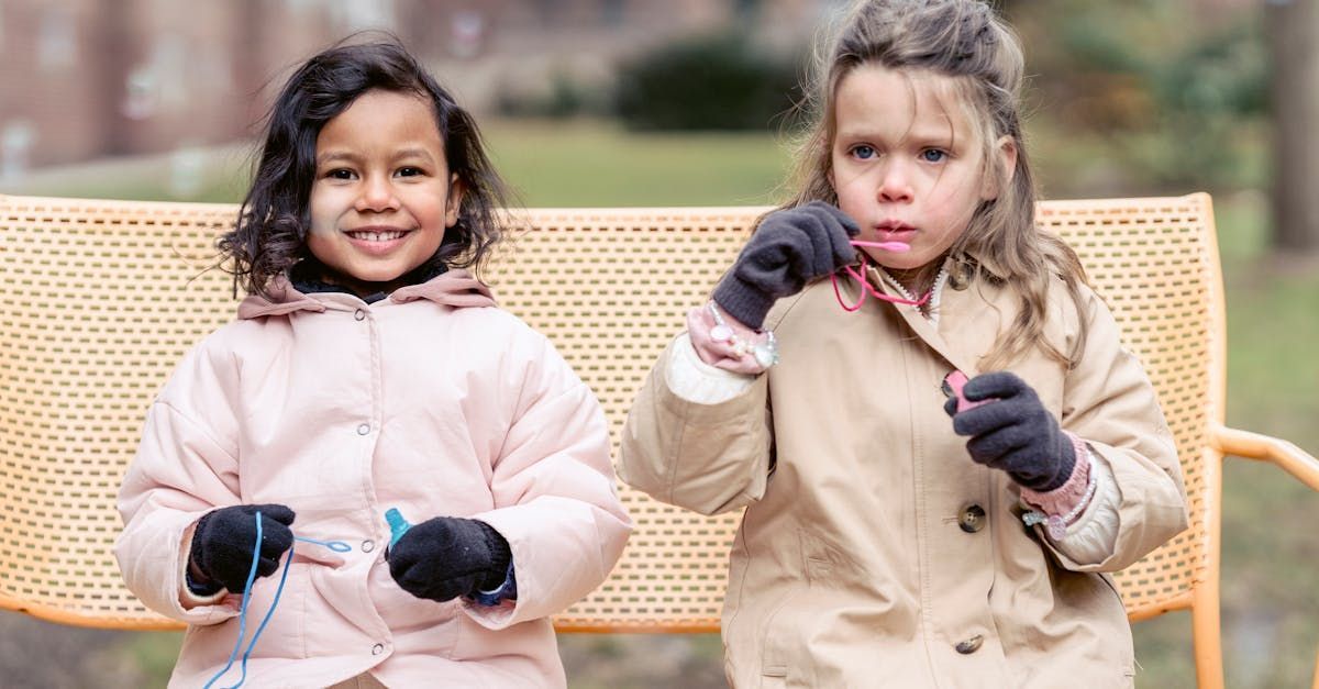 Two little girls are sitting on a bench in a park.