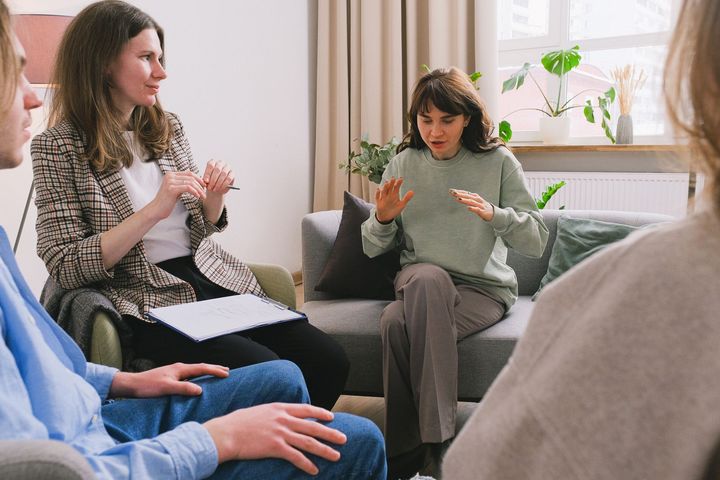 A group of people are sitting around a couch having a conversation.