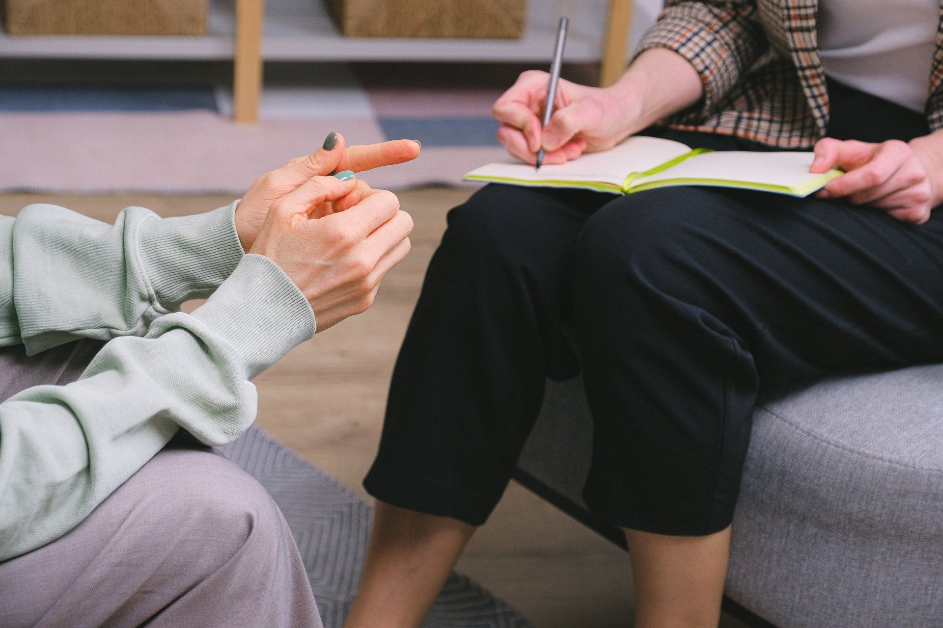 a woman is sitting on a couch talking to a man who is writing in a notebook .