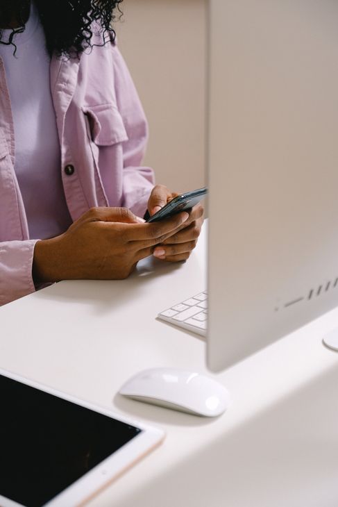 A woman is sitting at a desk using a cell phone.