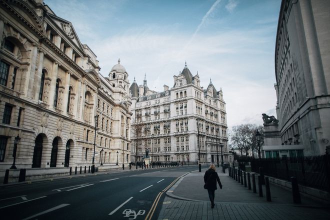 A man is walking down a street in front of a large building.