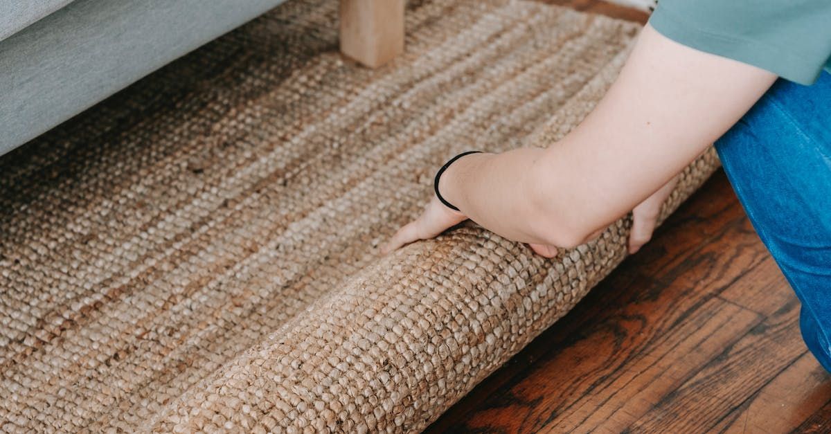 A person is laying a rug on the floor next to a couch.