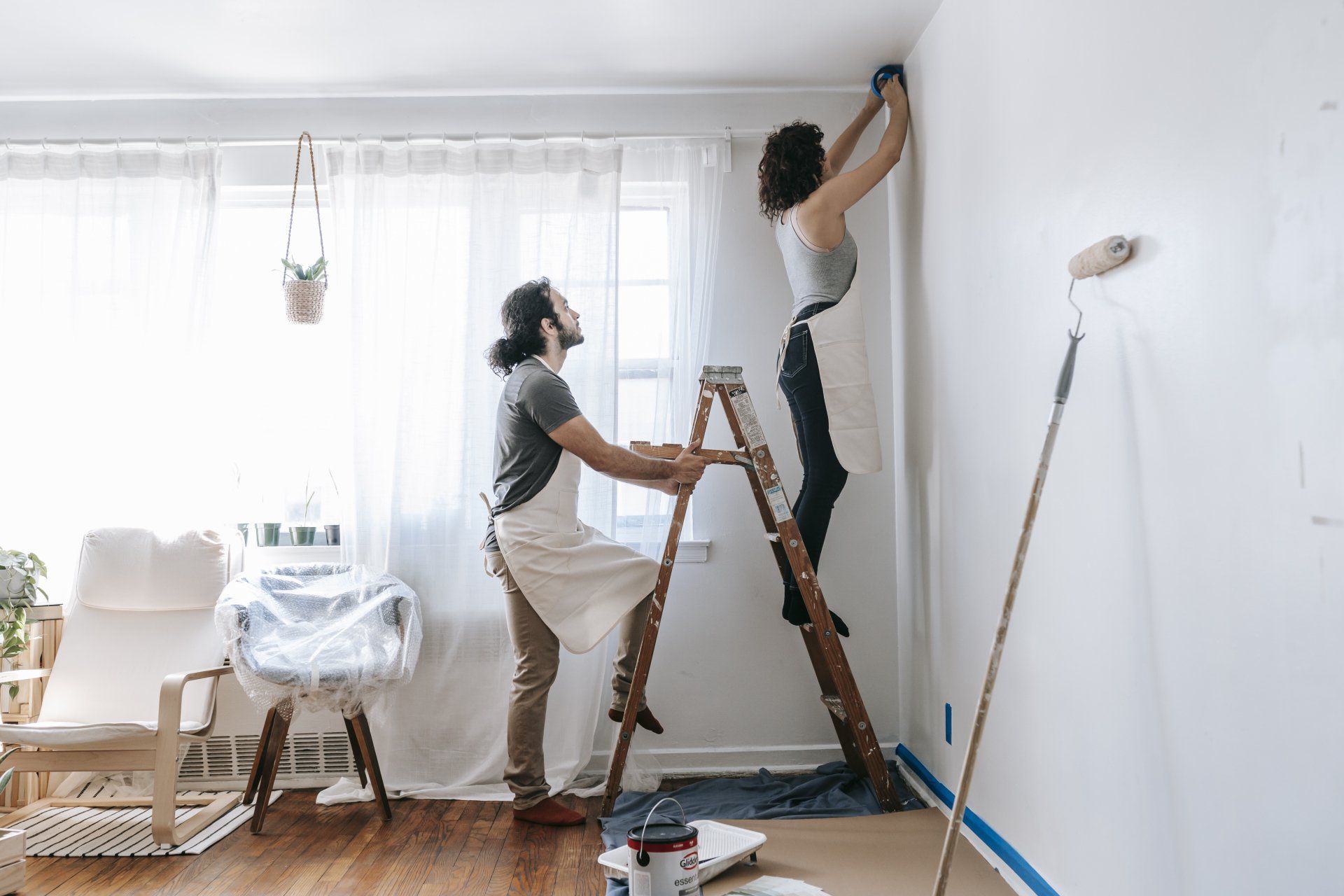a man and a woman are painting a wall in a living room
