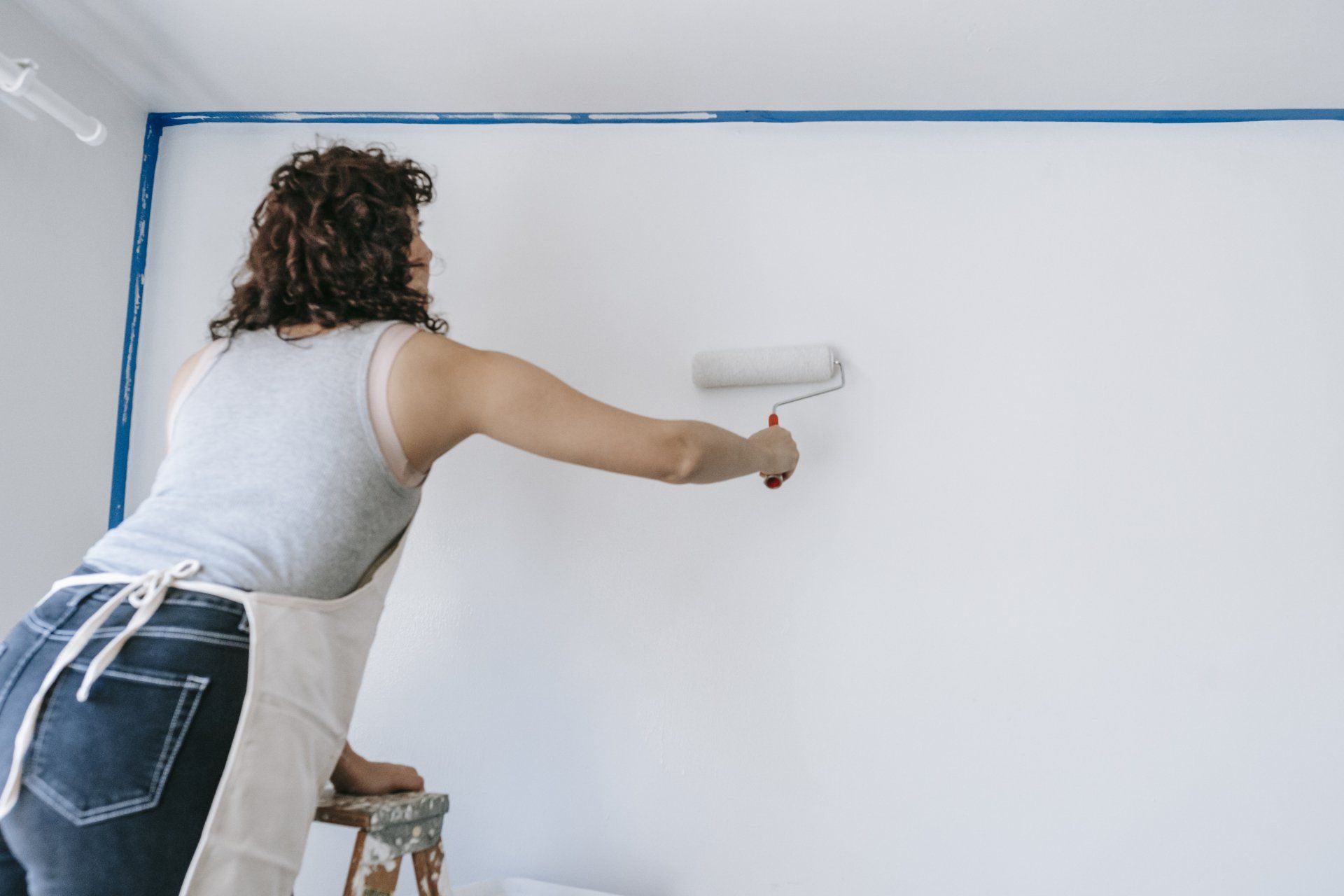 A woman paints a wall with primer and a roller brush