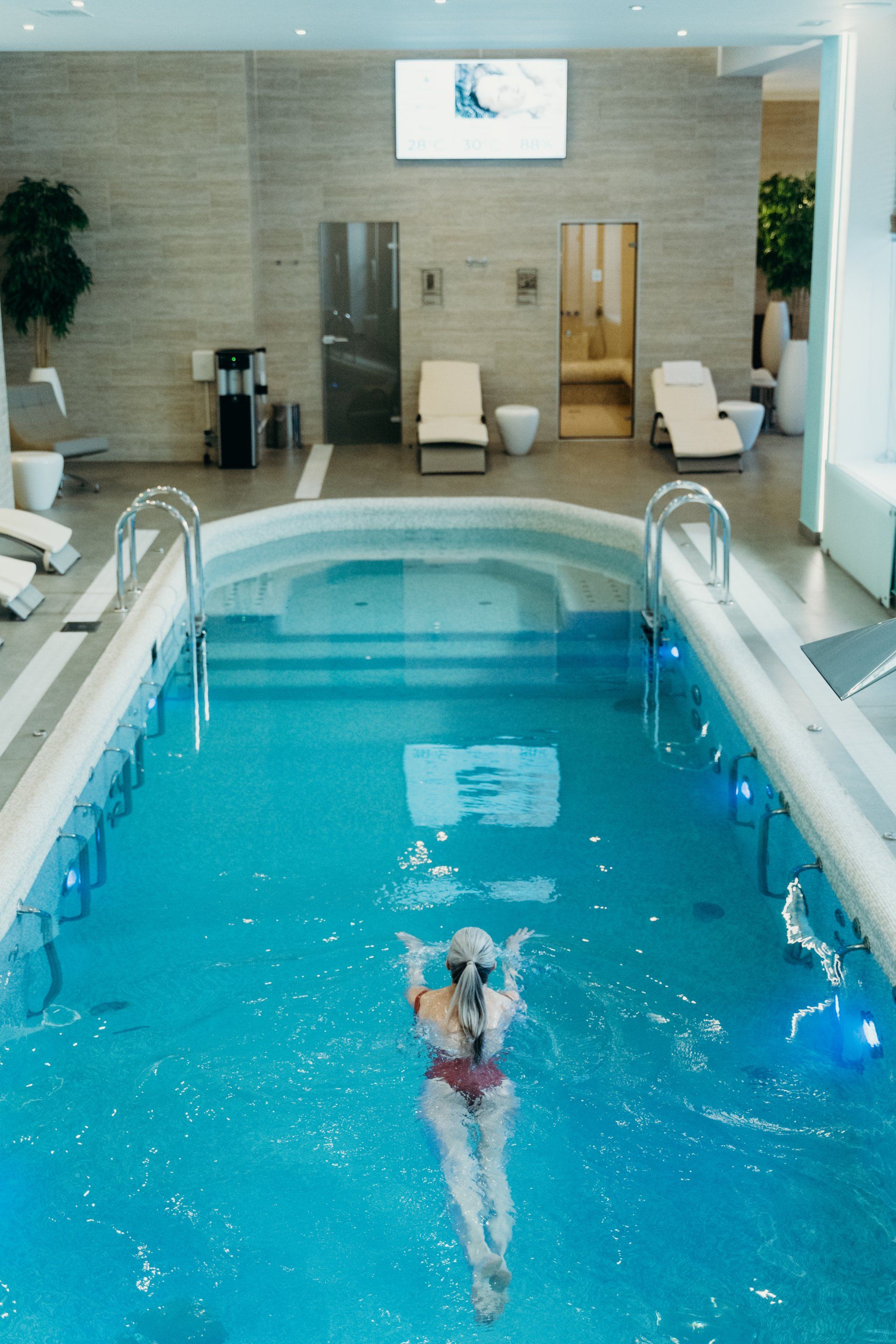 A woman is swimming in a large indoor swimming pool.
