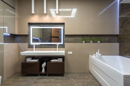 Small bathroom with white tube and dark wood vanity and lighted mirror