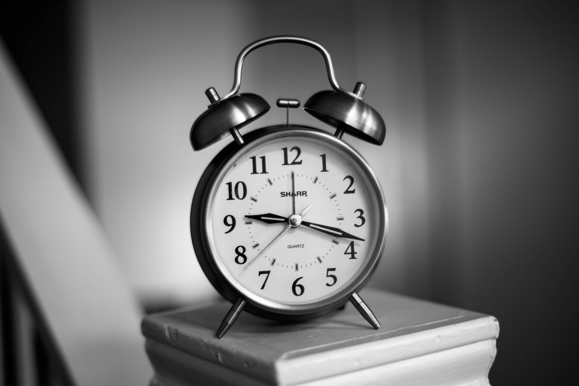 A black and white photo of an alarm clock on a pedestal.