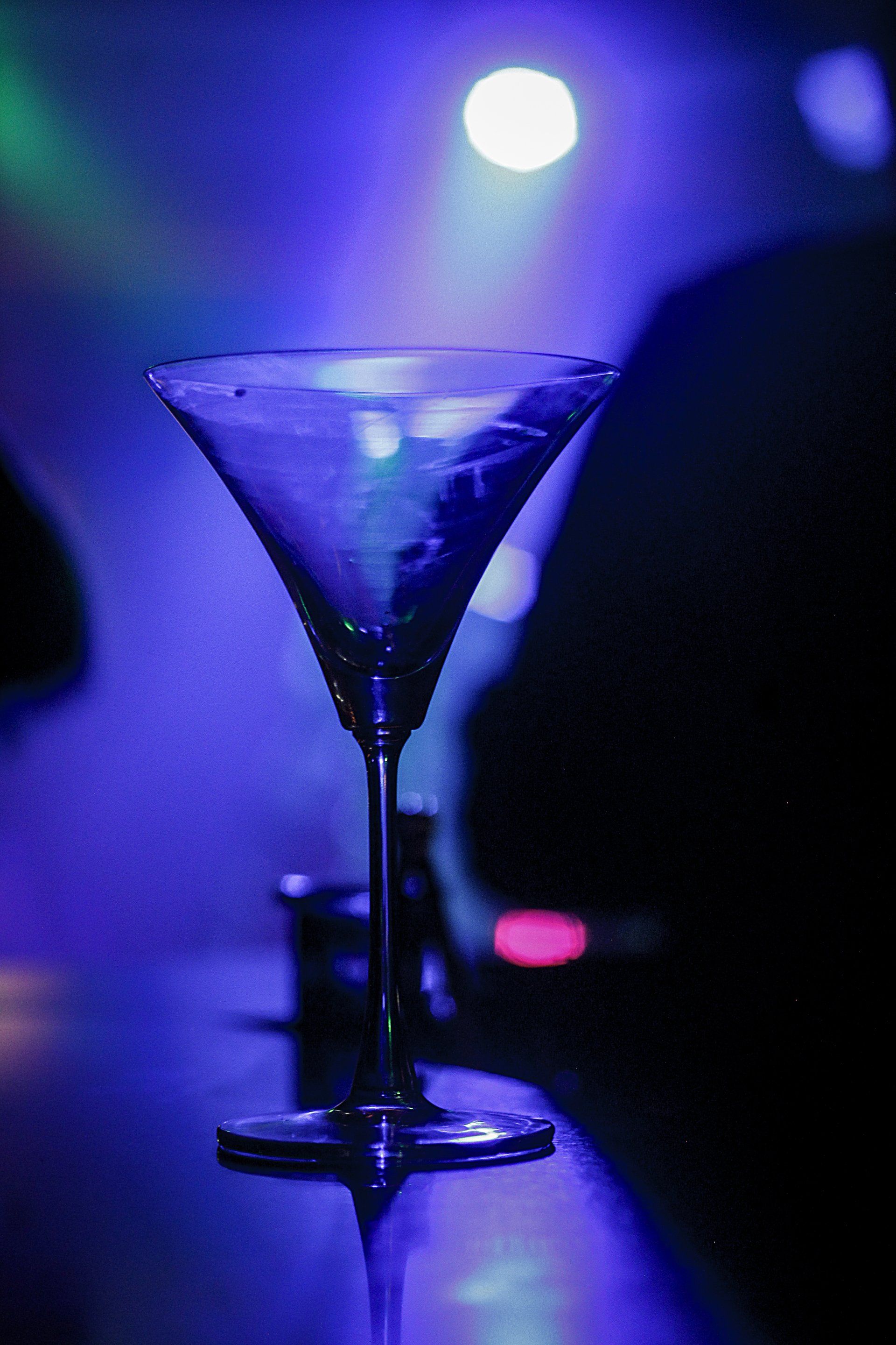 A martini glass filled with a blue liquid is sitting on a bar.