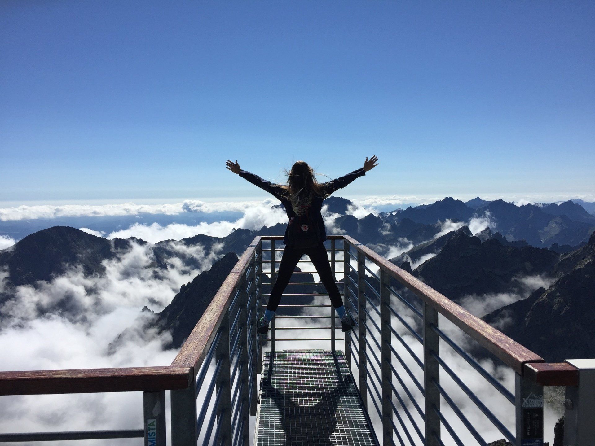 a woman is standing on a balcony overlooking mountains with her arms outstretched