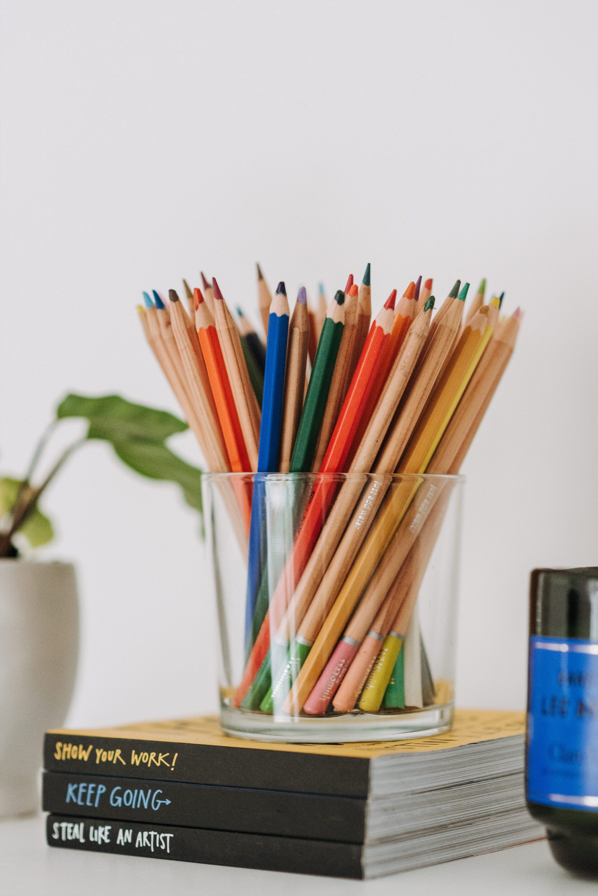 A glass filled with colored pencils is sitting on top of a stack of books.