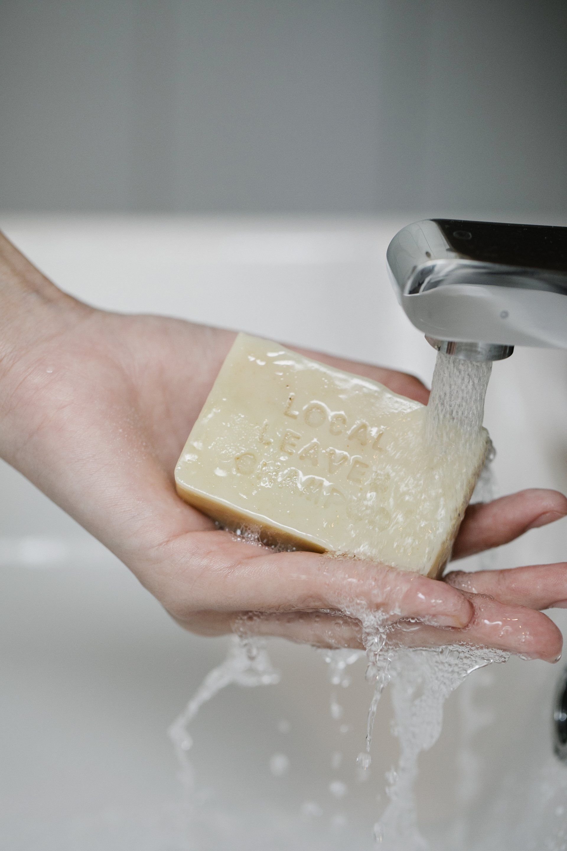 Person holding bar of soap under running water in a white sink.