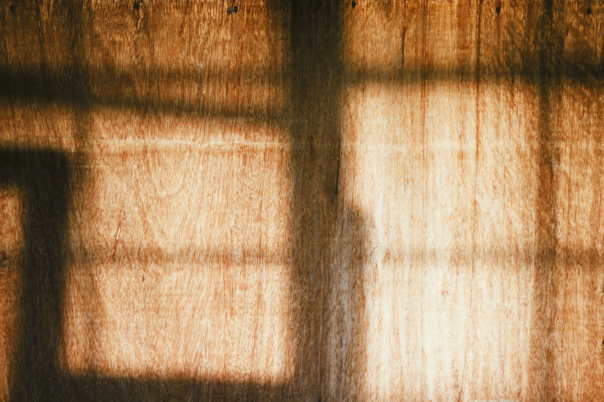 The shadow of a window is cast on a wooden wall.