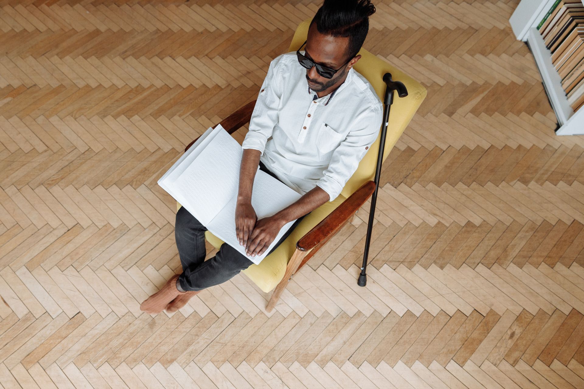 A blind man is sitting in a chair reading a book.