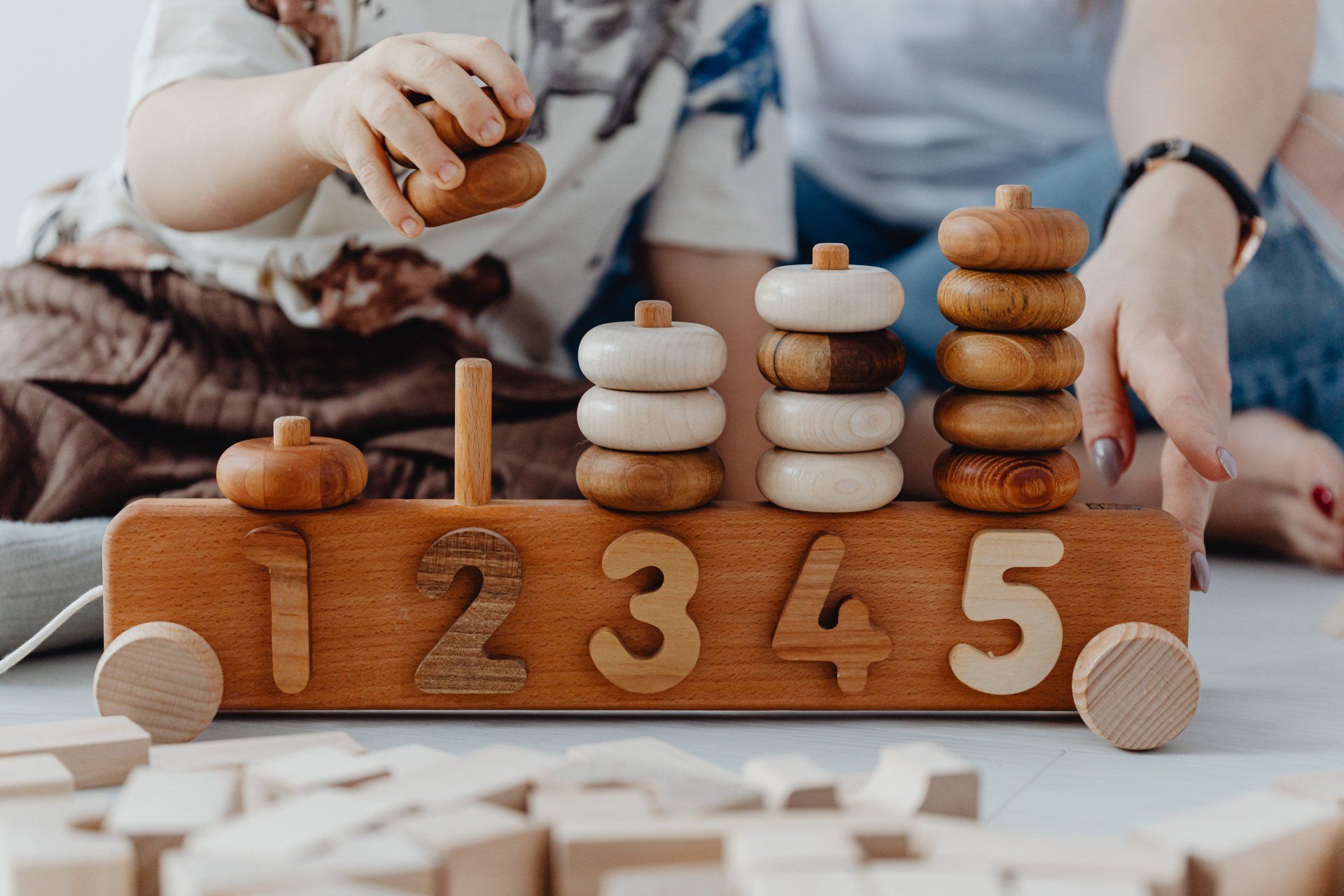 A child and adult play with a wooden toy train featuring numbered pegs stacked with rings.