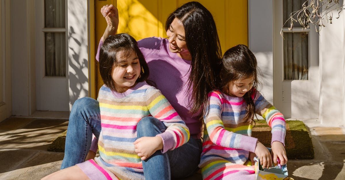 A woman and two girls are sitting on the ground in front of a yellow door.