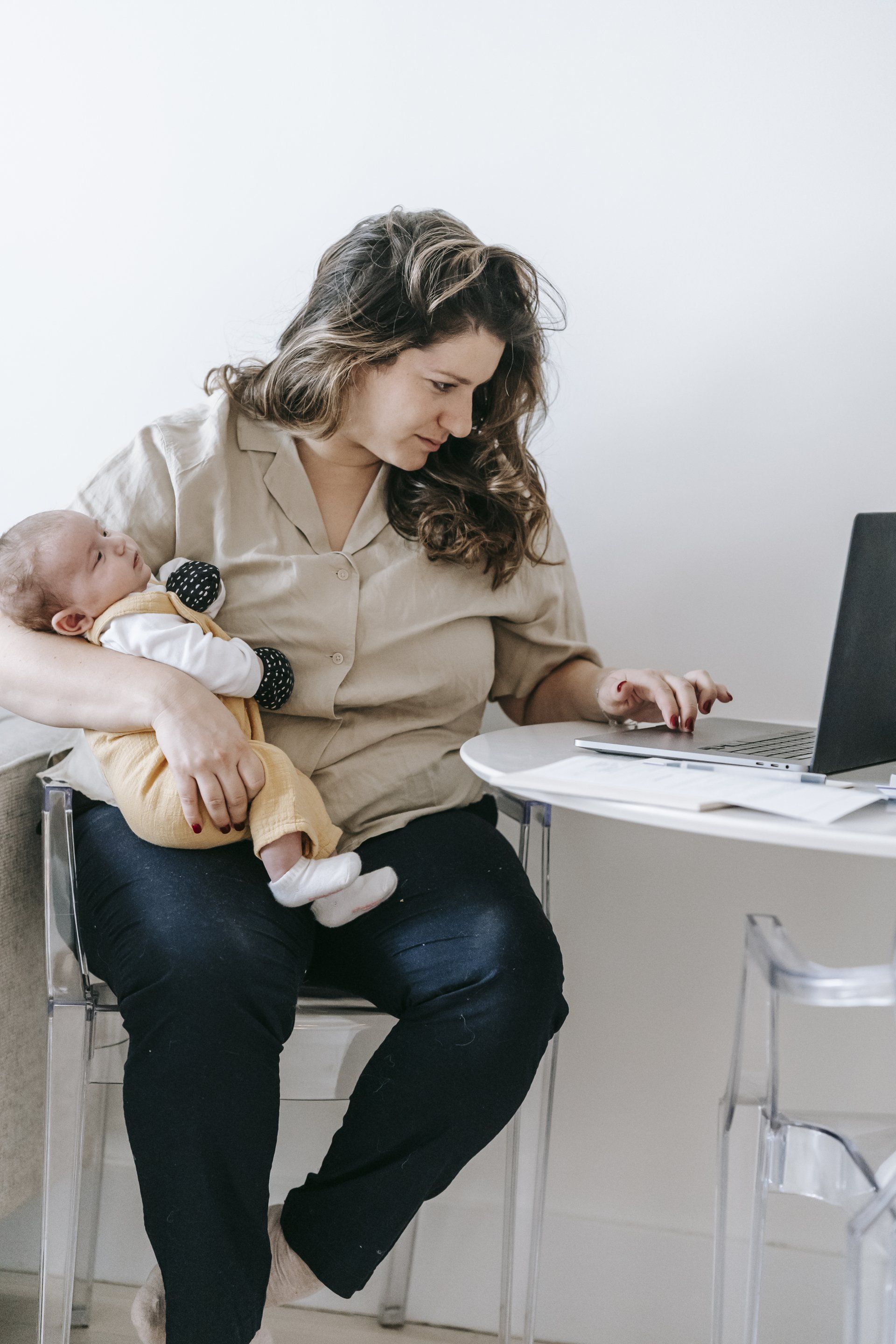 A Woman holding her baby while working on a laptop