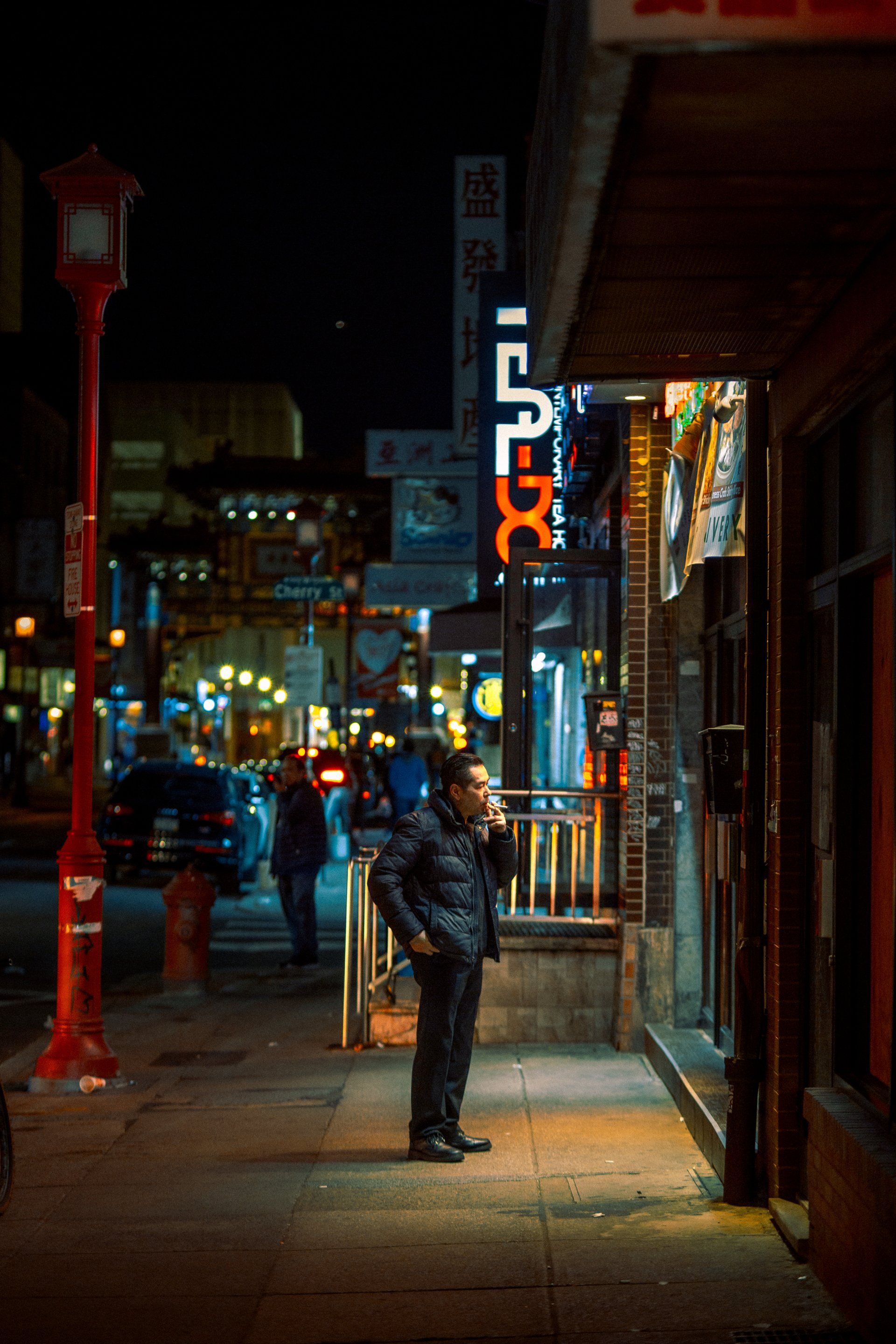 A man is standing on a sidewalk in front of a building at night.