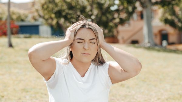 A woman is sitting in the grass with her hands on her head.