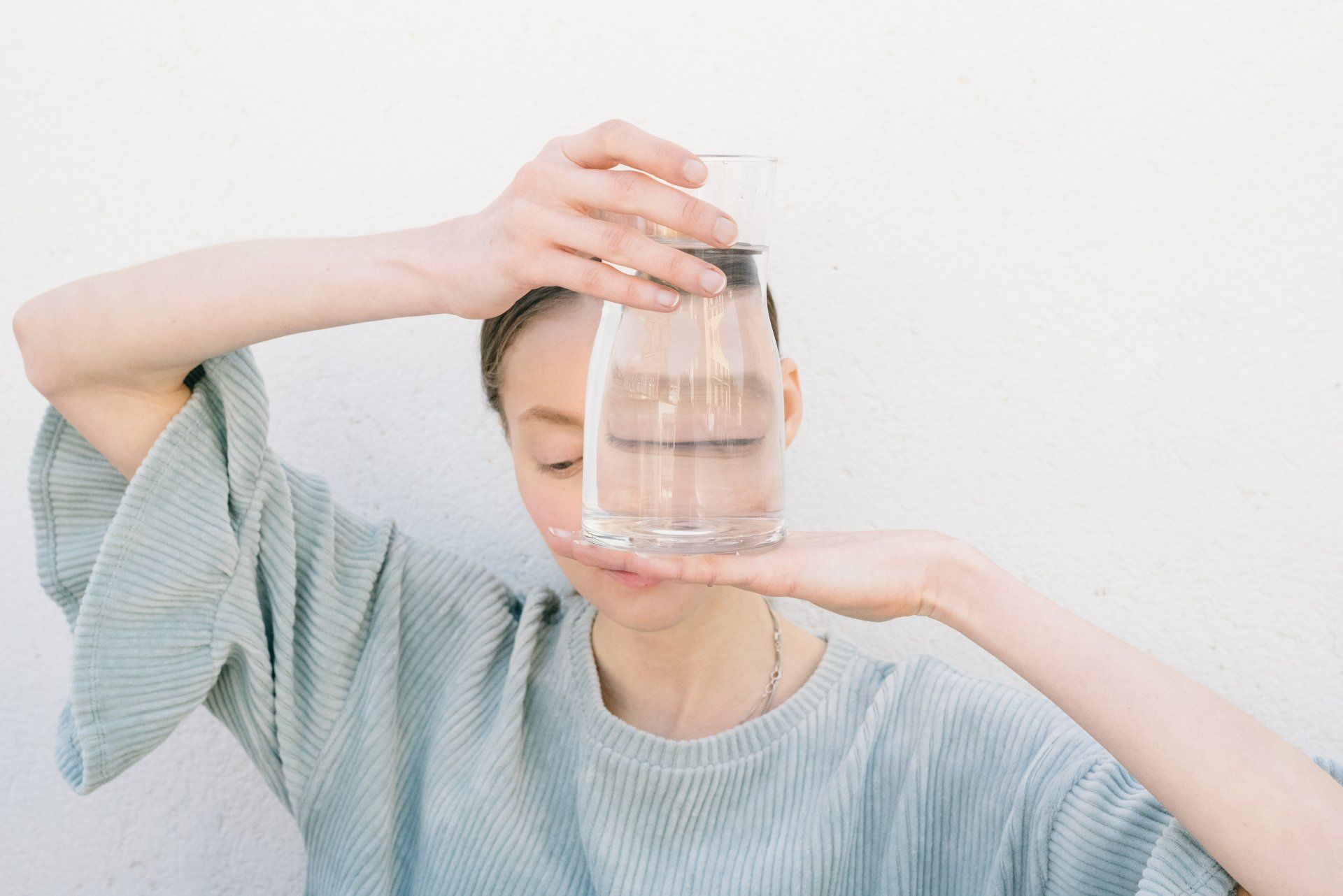 A woman holding a caraf of water in front of her face.
