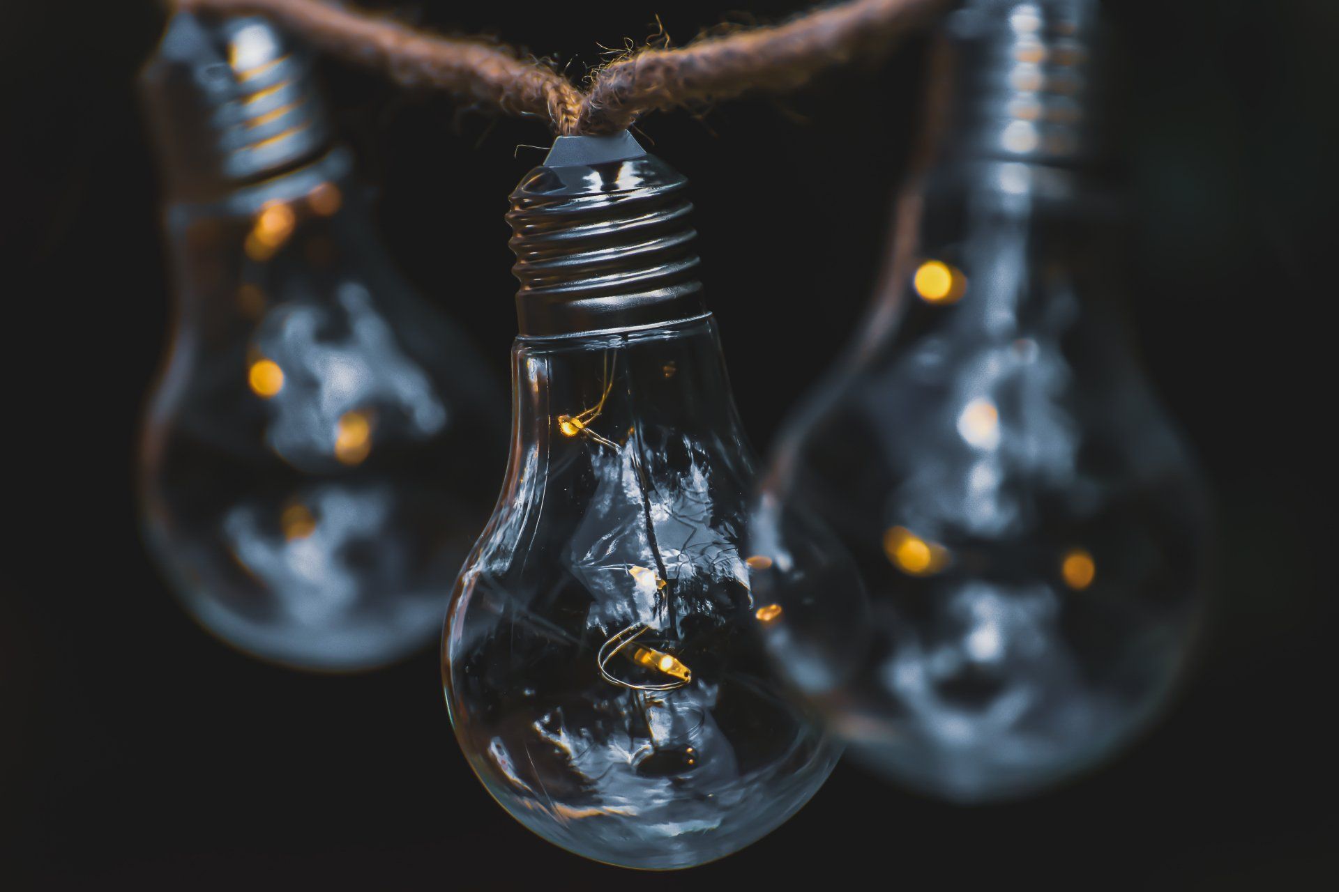 Three clear light bulbs hanging from a string against a black background.