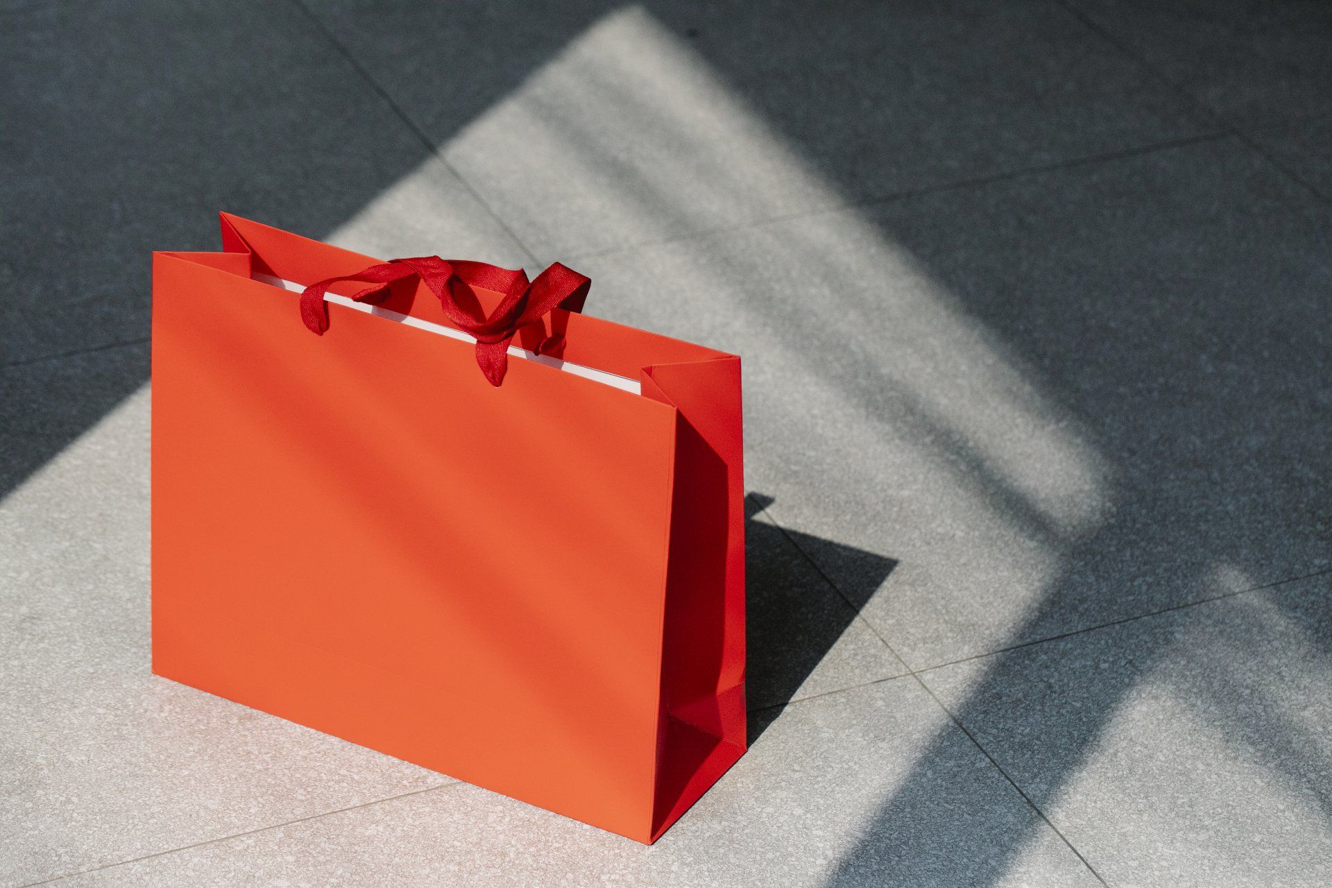 a red shopping bag with a red bow is sitting on the floor 