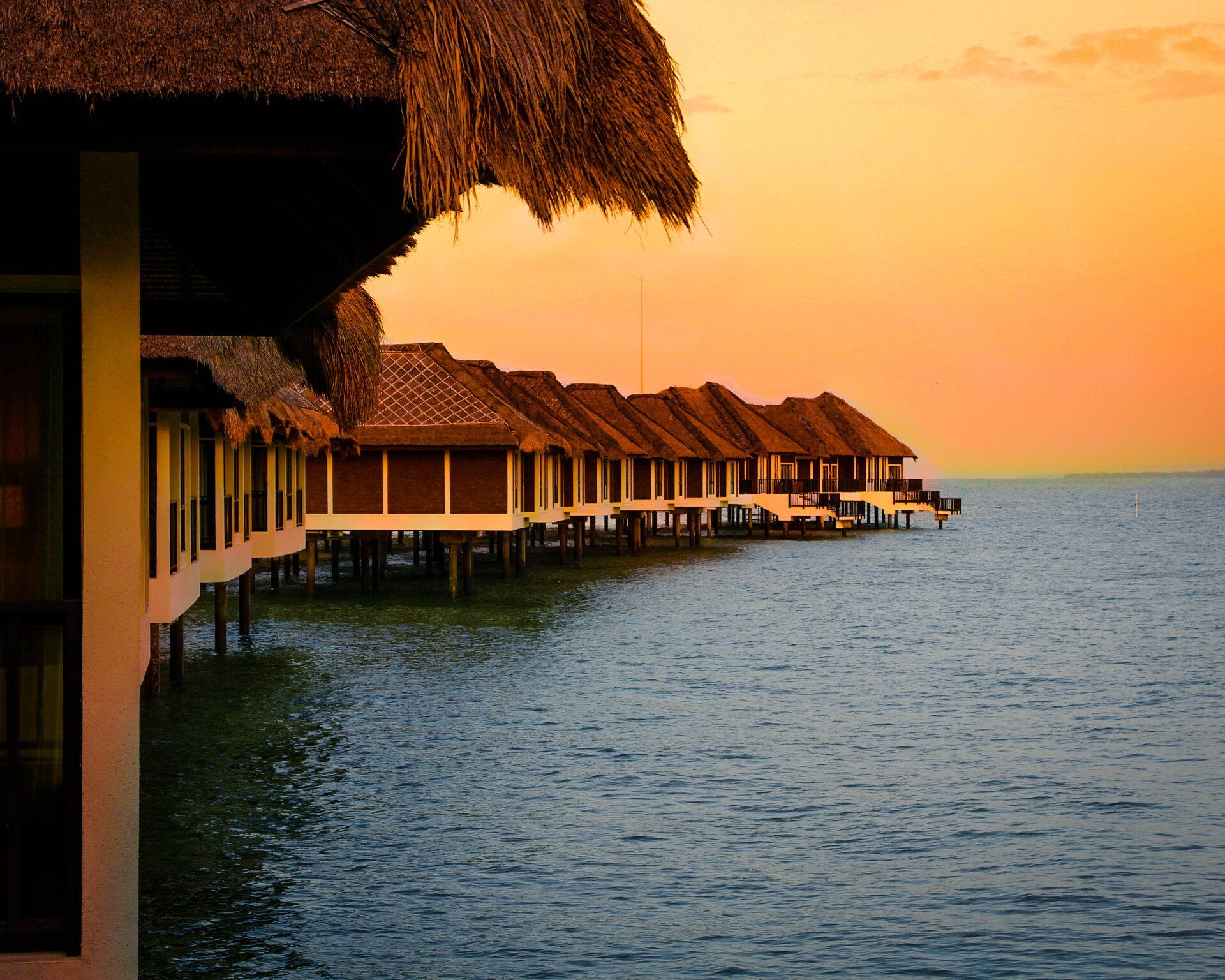 A row of huts on stilts overlooking the ocean at sunset