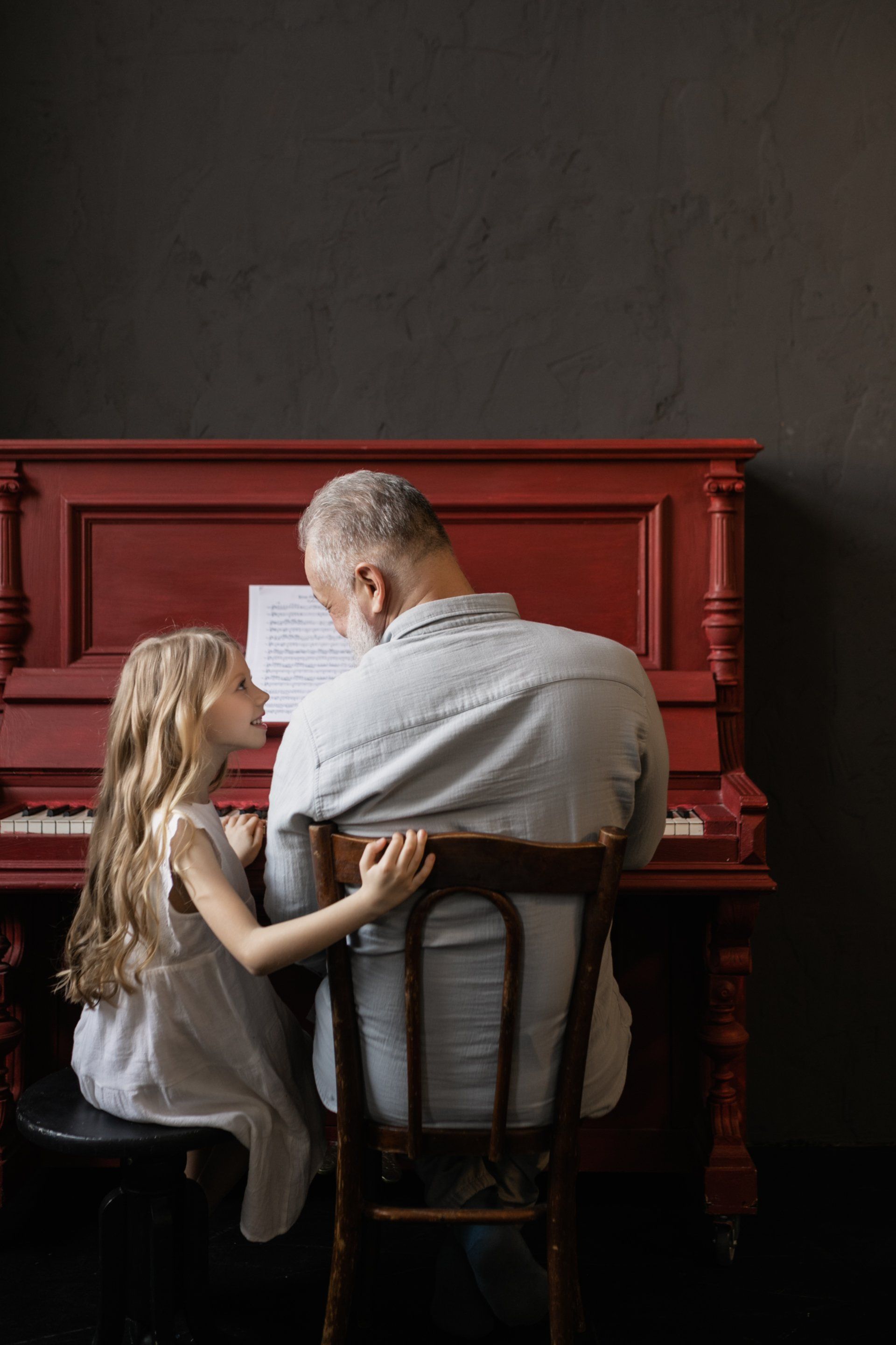 a man and a little girl are sitting at a red piano .