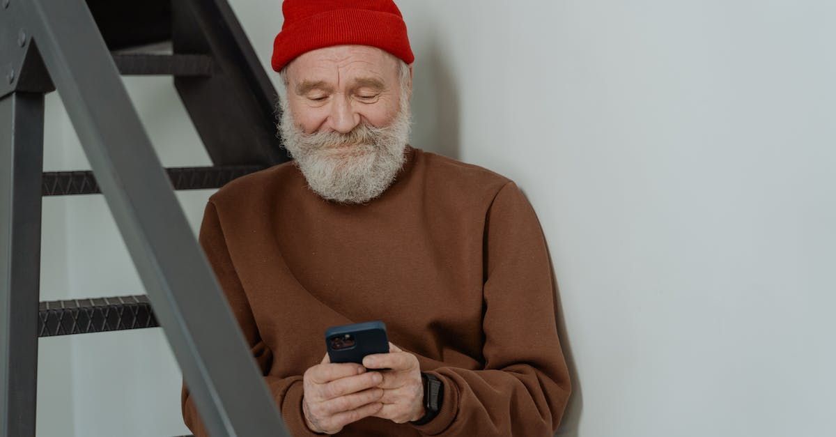 An elderly man with a beard is sitting on the stairs using a cell phone.