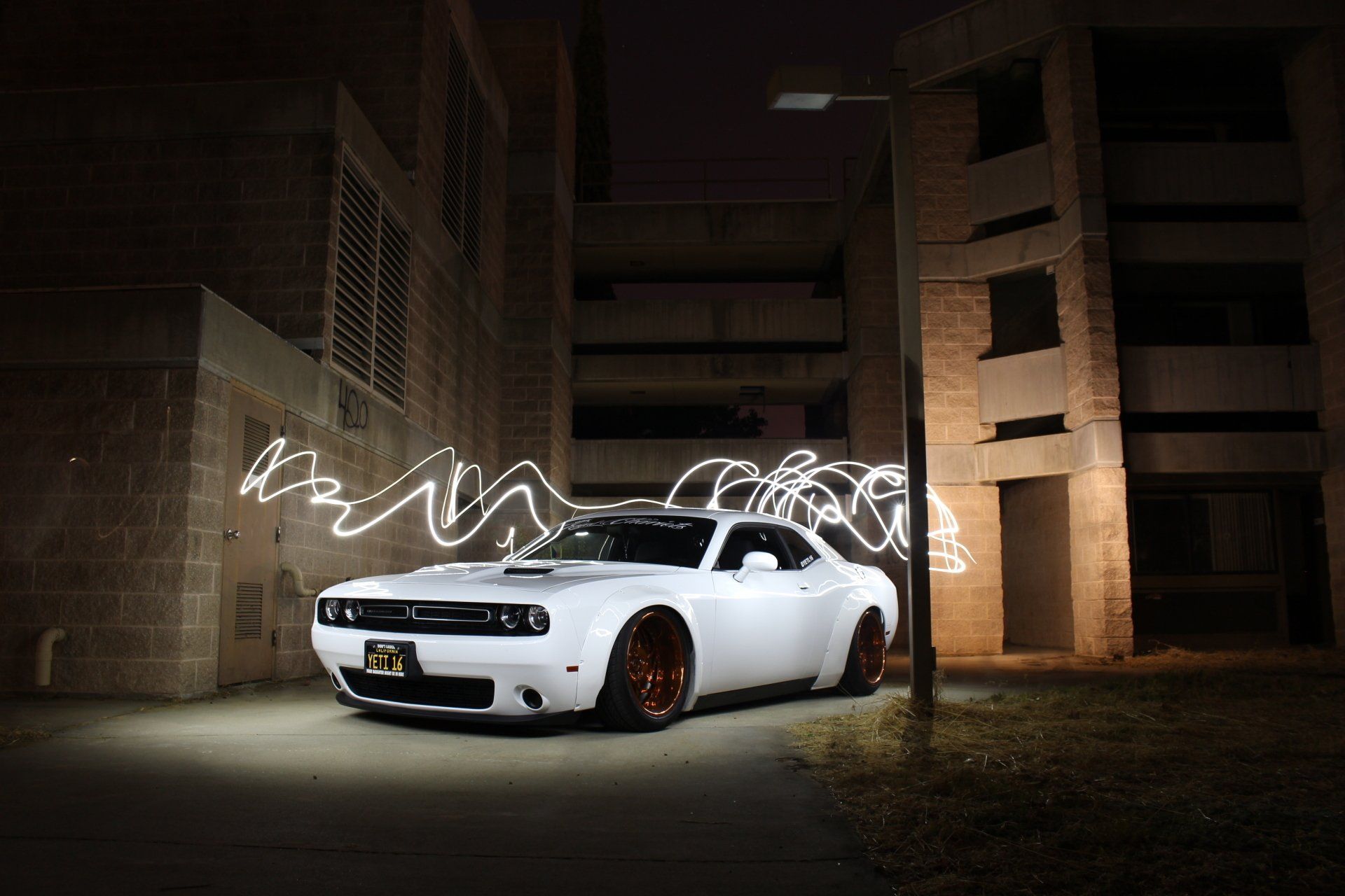 a white dodge challenger is parked in front of a building at night .