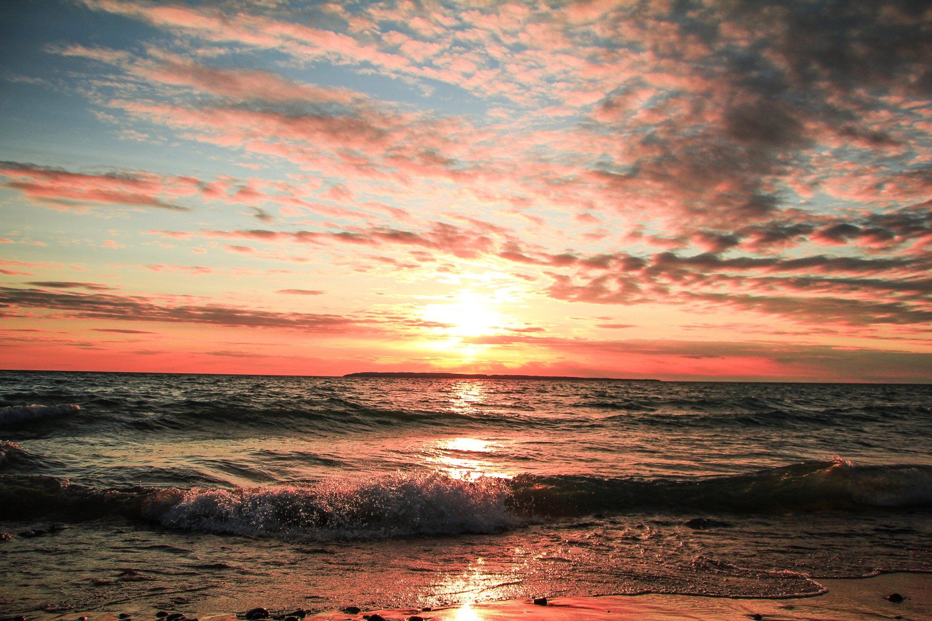 The sun is setting over the ocean and the waves are crashing on the beach.