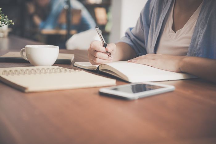 Una mujer está sentada en una mesa escribiendo en un cuaderno.