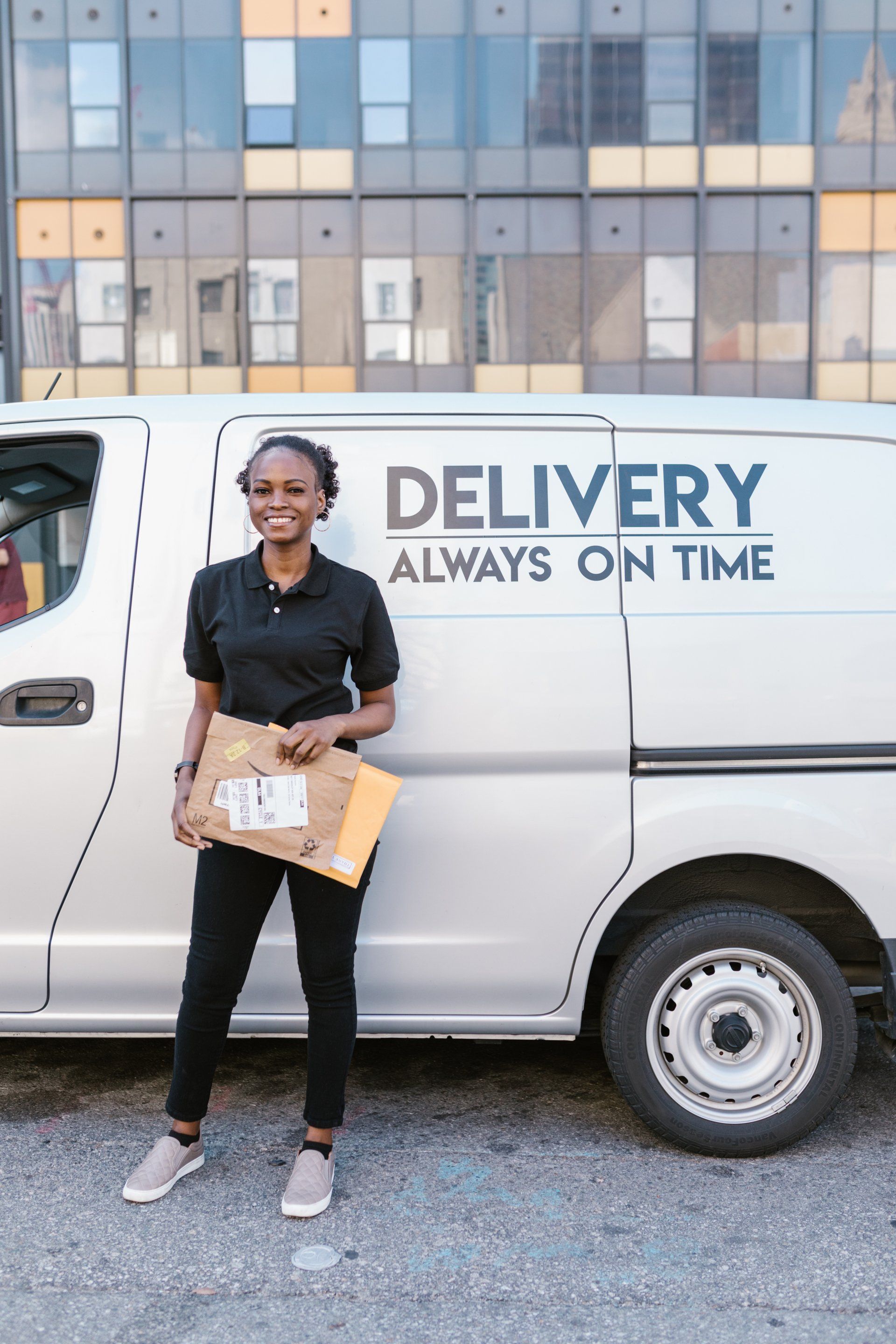 a delivery woman is standing in front of a delivery van holding a package .