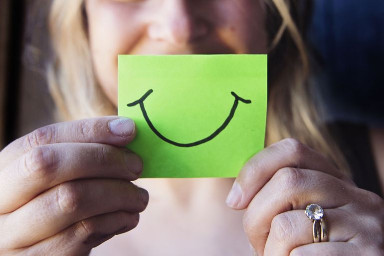 A person holding a post-it note with smiley writing on it.