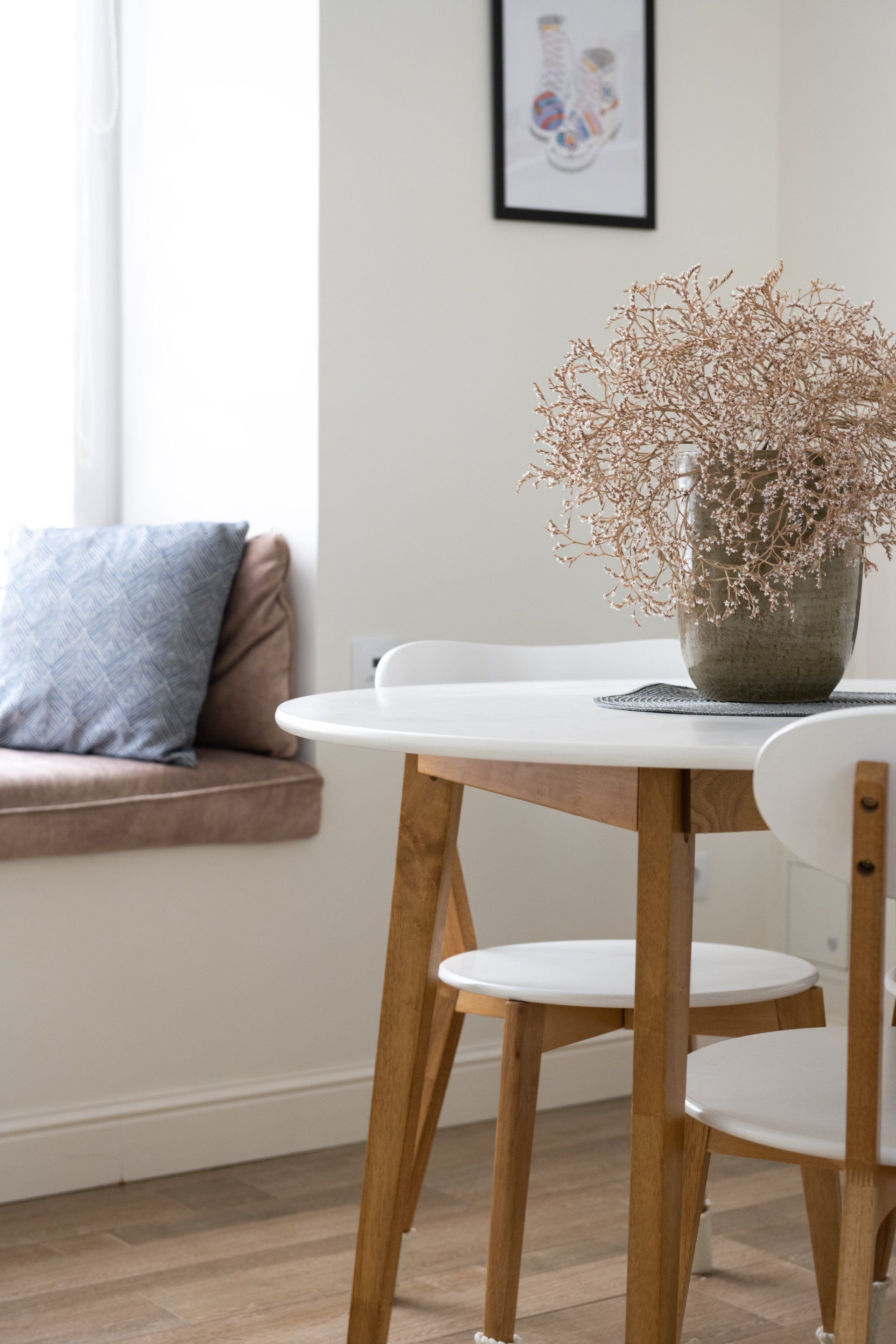 A dining room table and chairs with a vase of dried flowers on it.