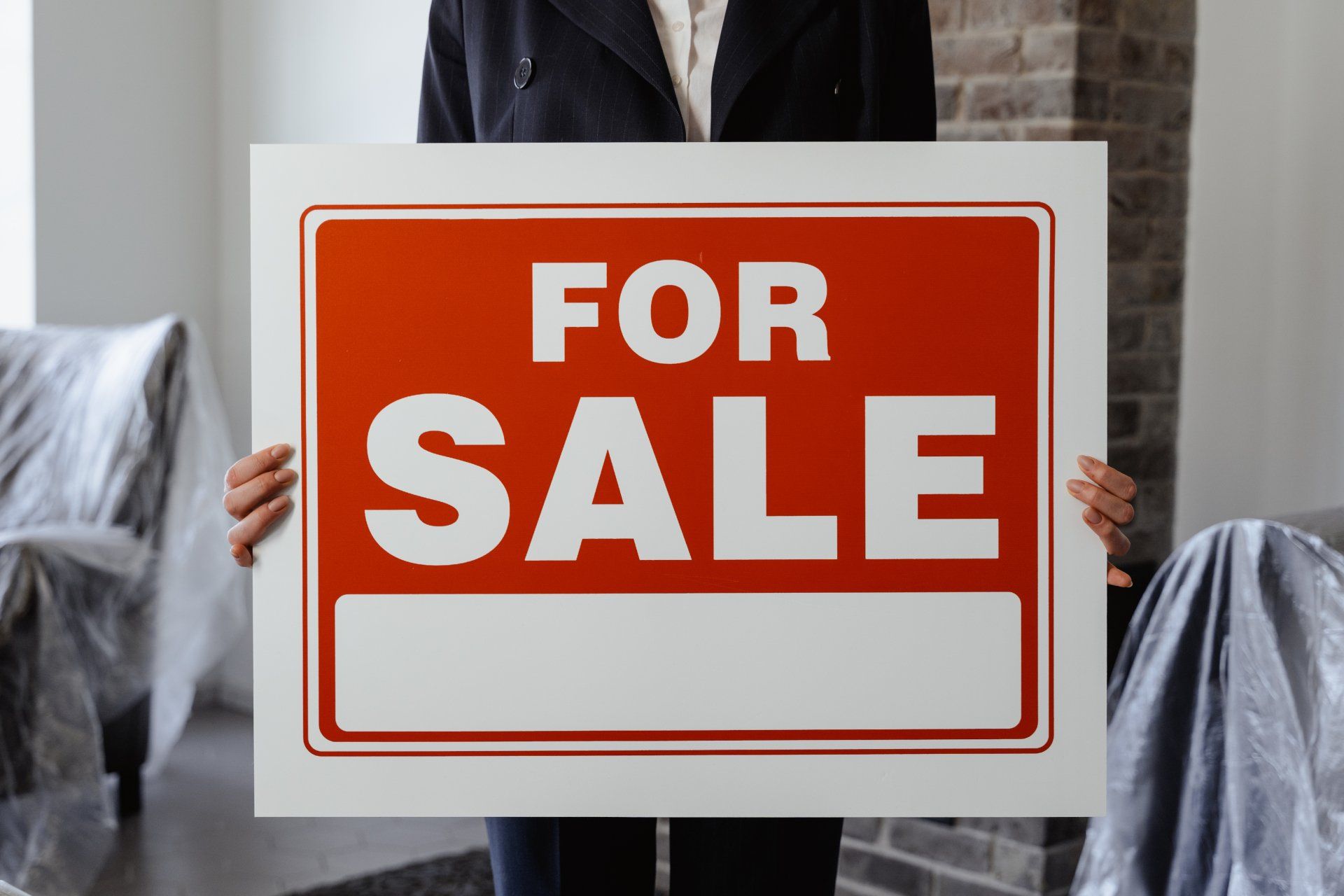 A woman is holding a for sale sign in a living room.