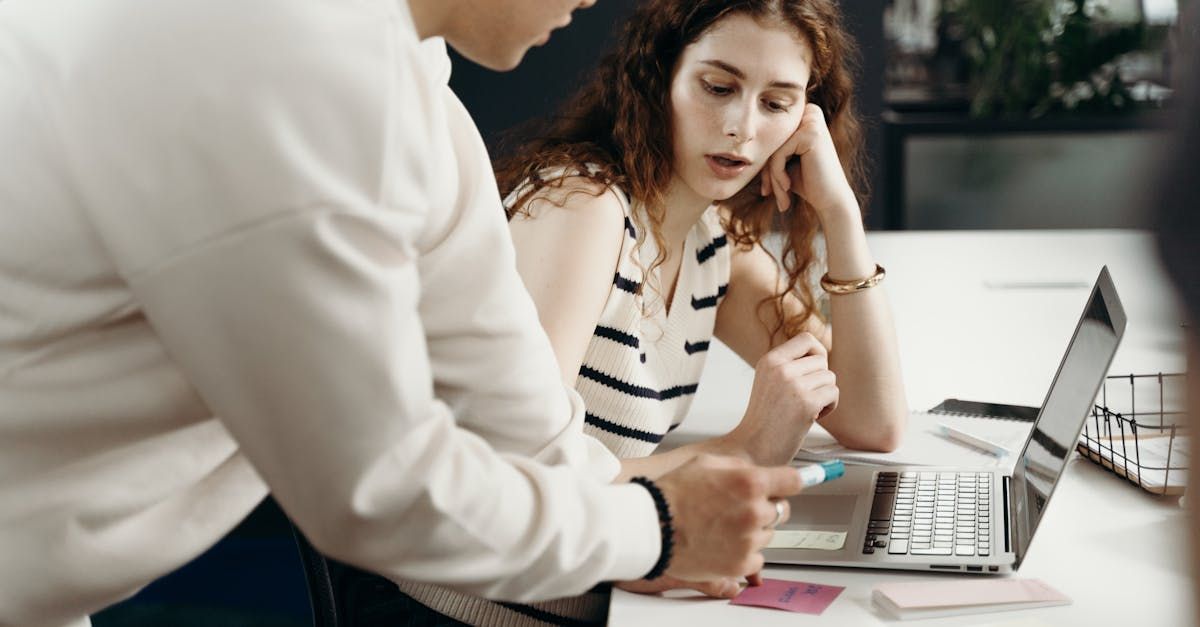 A man and a woman are sitting at a table looking at a laptop.
