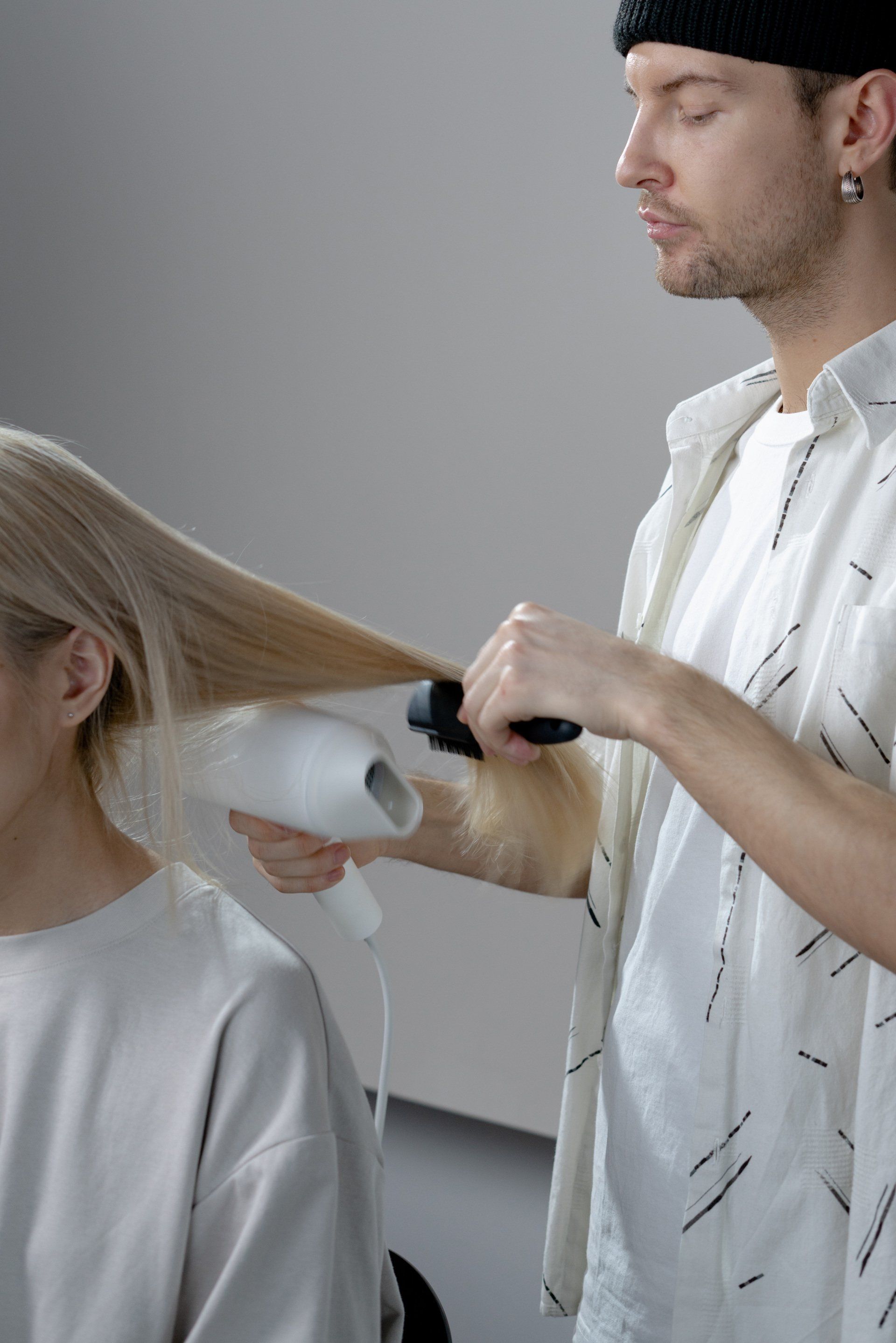 Imagem de um homem secando o cabelo de uma mulher loira no salão de beleza