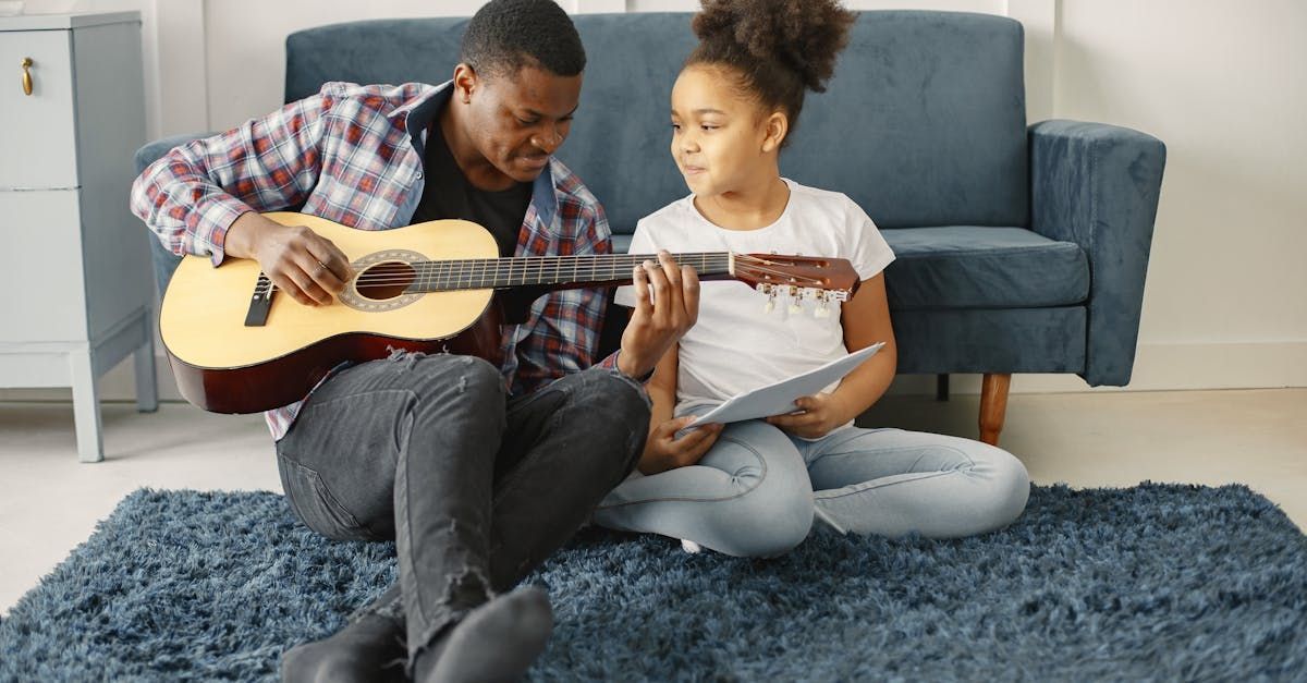 child sitting next to adult male who is playing guitar against a couch