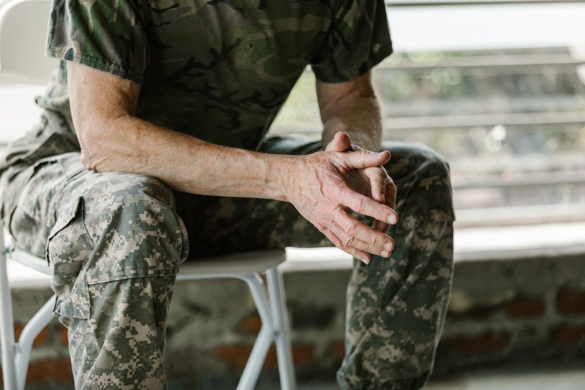 Sitting man in army fatigues leaning forward with elbows on legs