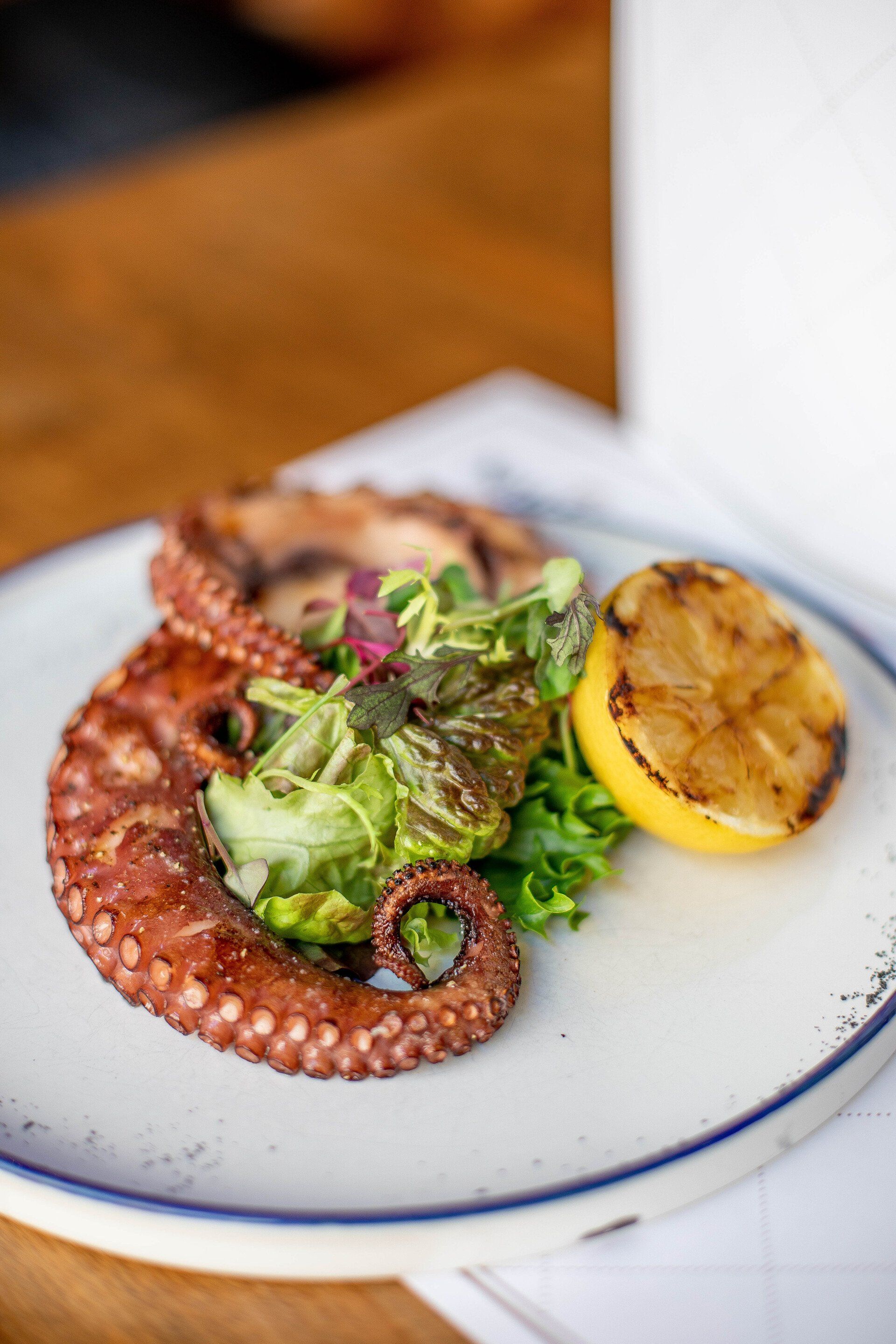 A close up of a plate of food with an octopus and a lemon on a table.