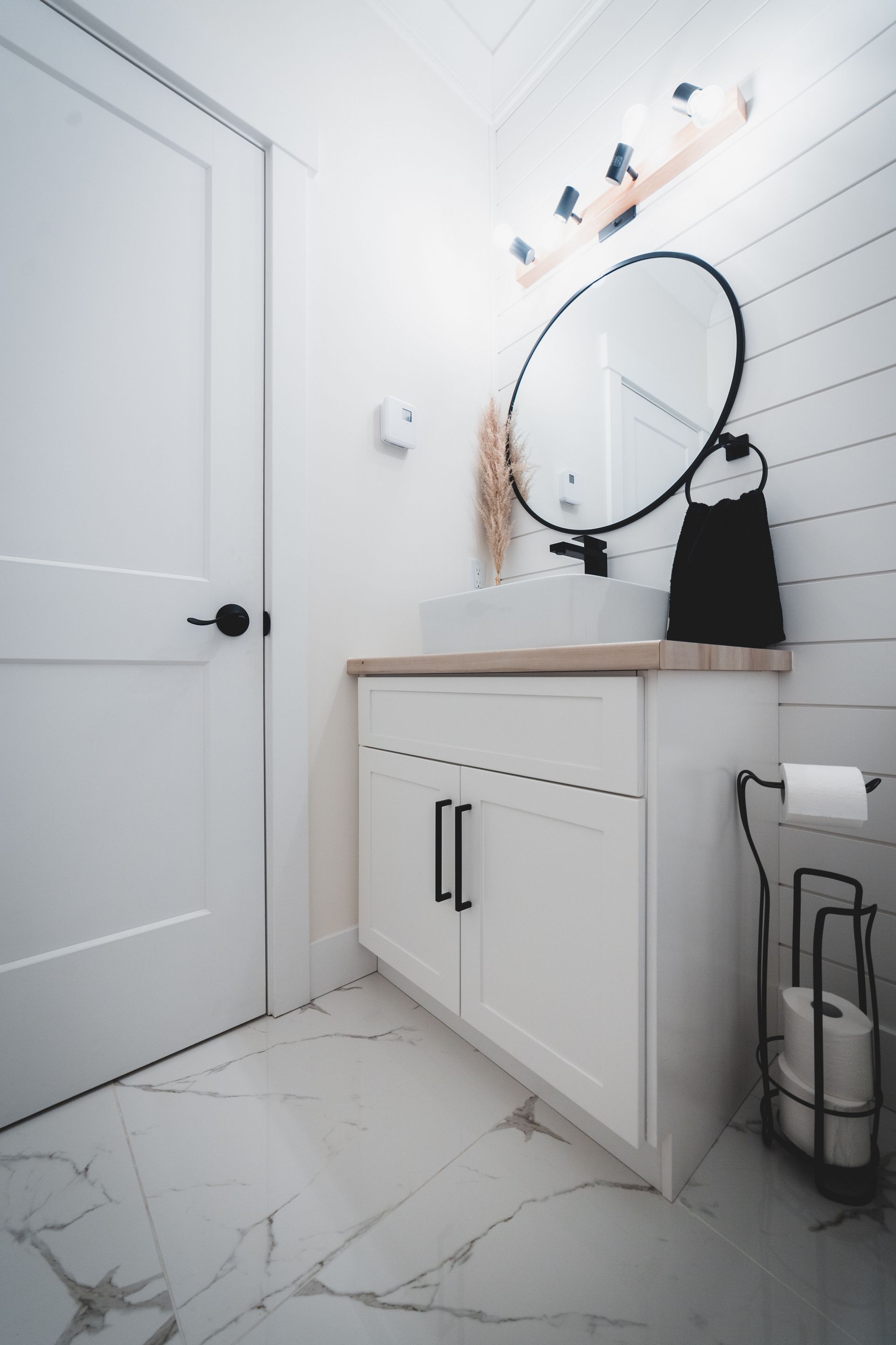White bathroom with a vanity, round mirror, and black fixtures.